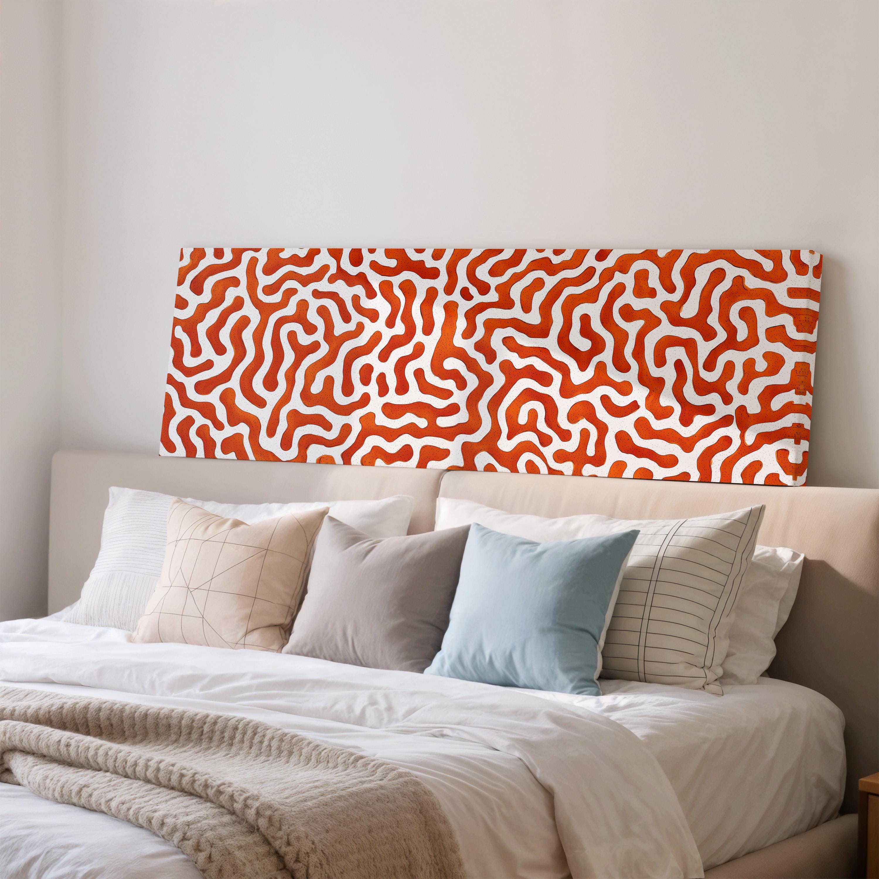 a well-made bed with a white comforter and a variety of pillows in different colors and patterns. The bed is positioned against a wall with a large, abstract orange and white patterned headboard.