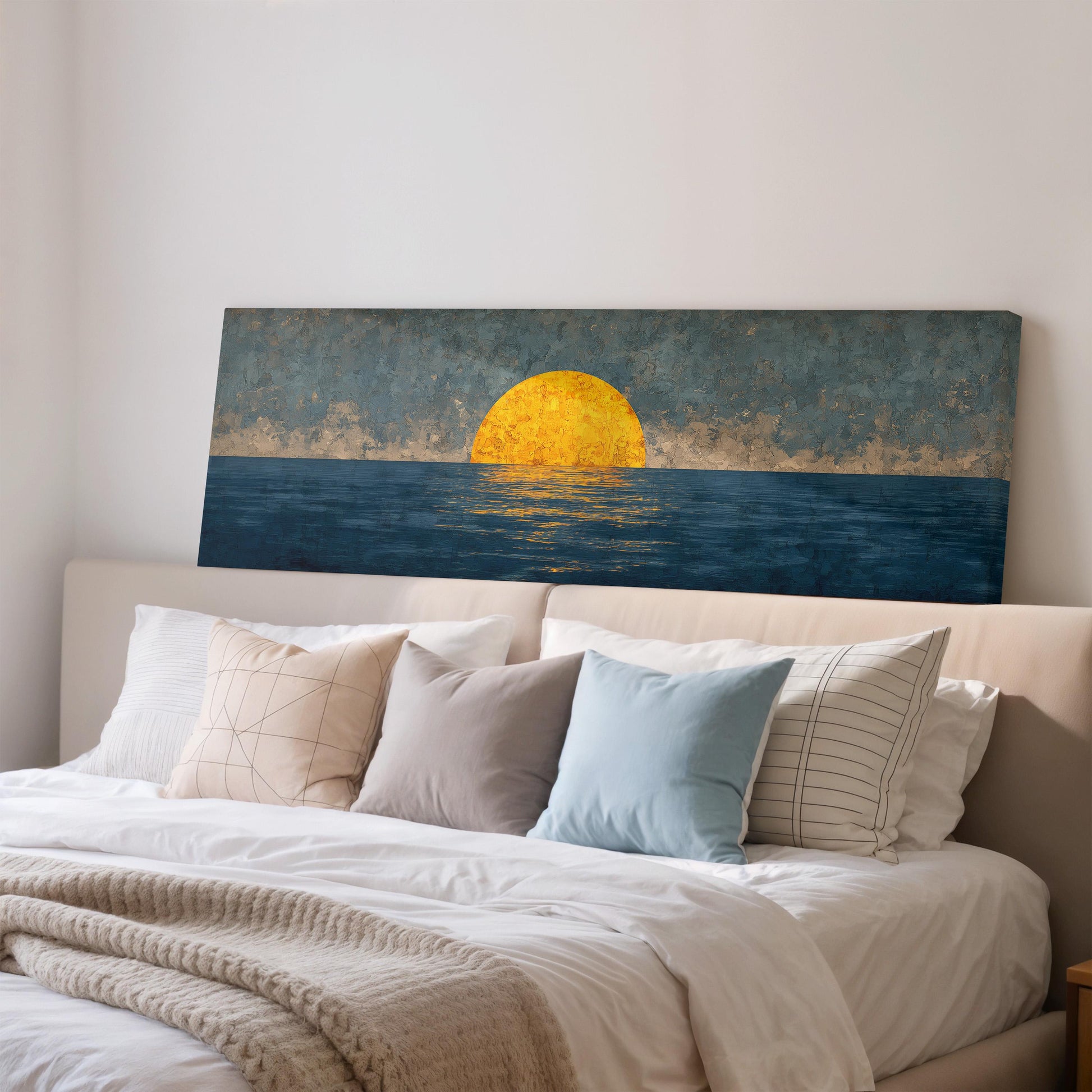 a large painting of a sunset over the ocean, hanging on a wall above a bed with white pillows and a gray blanket.