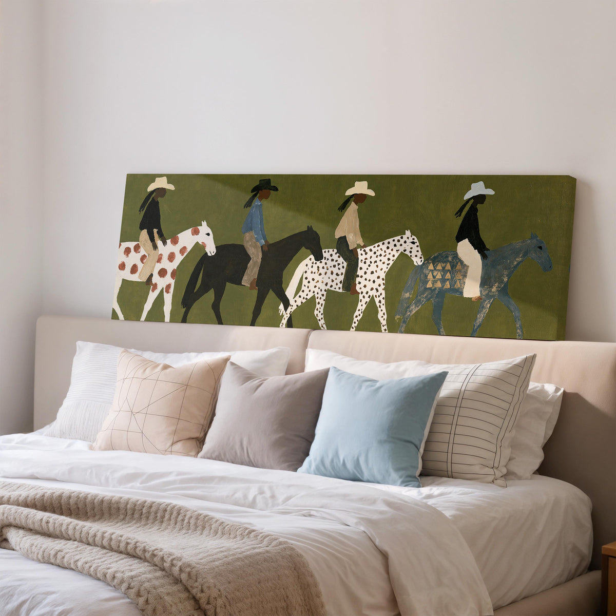 Riders on spotted ponies on olive green wide panoramic canvas print above a bed in a bedroom