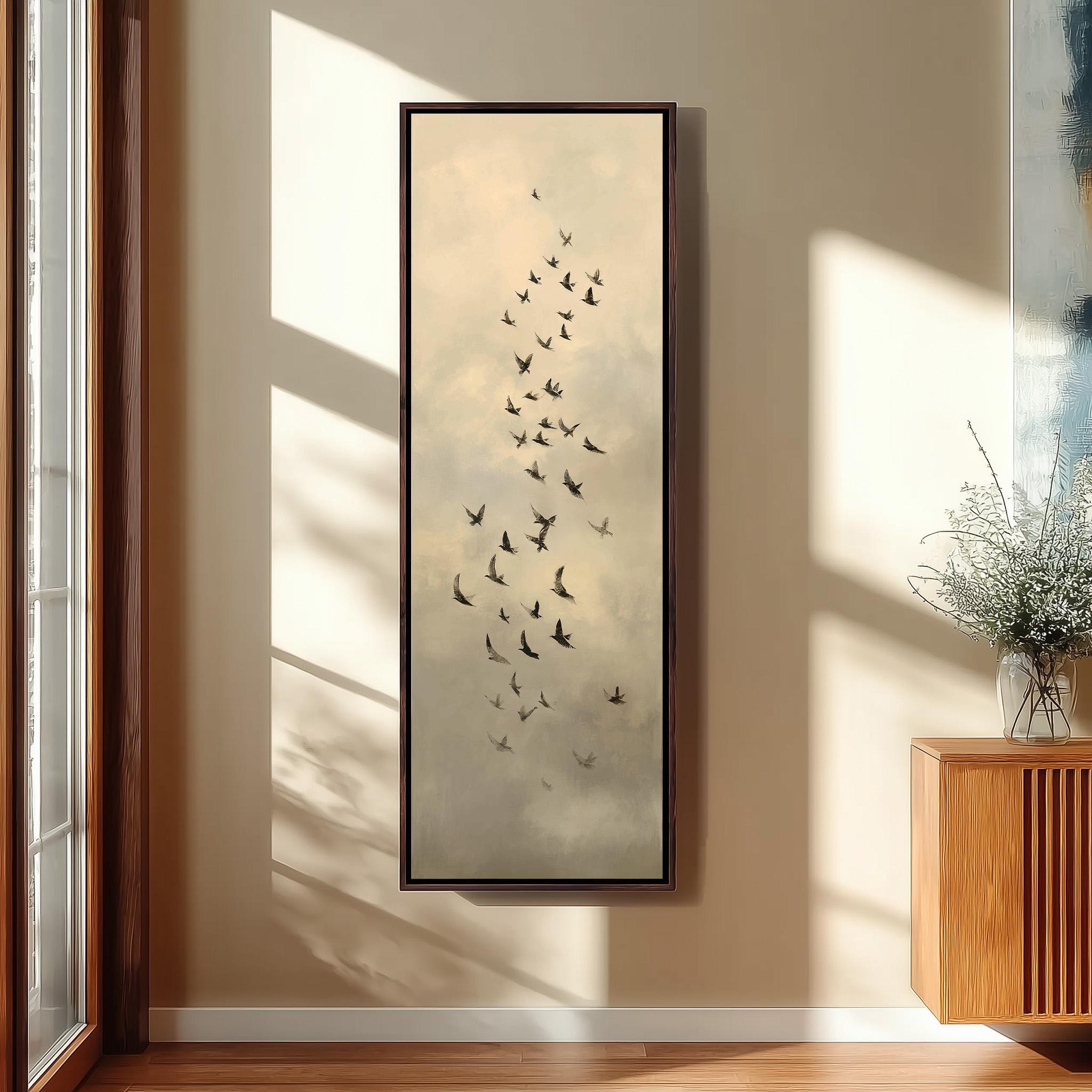 a large framed painting of a flock of birds flying in the sky, hanging on a wall in a room with a wooden cabinet below it.