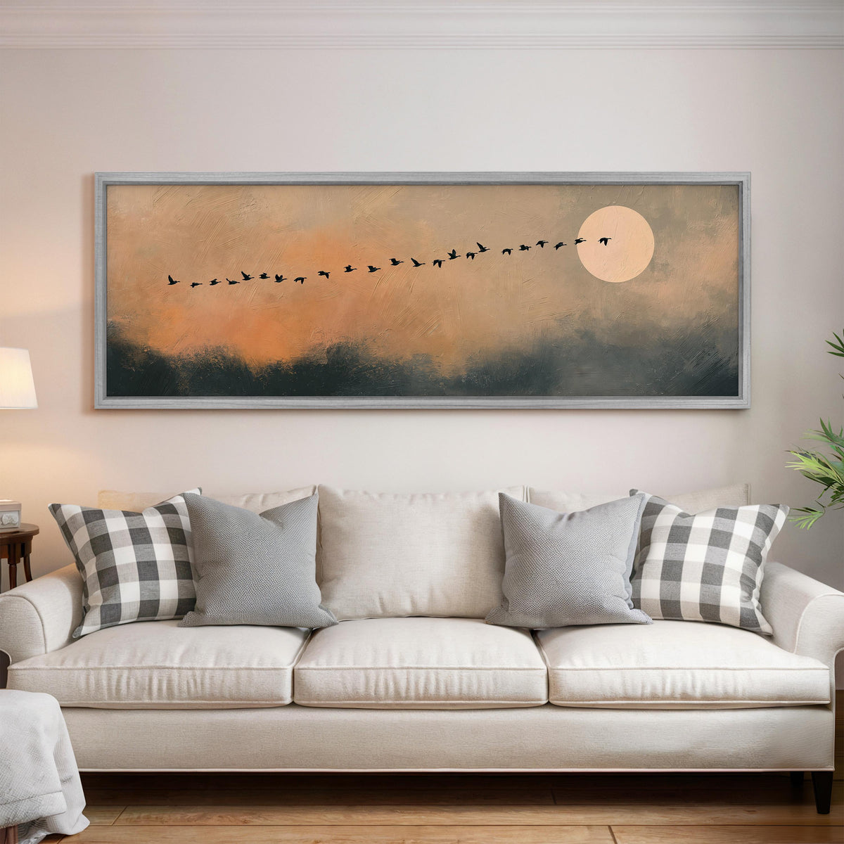Migrating birds passing a moon at peach dusk panoramic canvas print above a white sofa in a bright living room