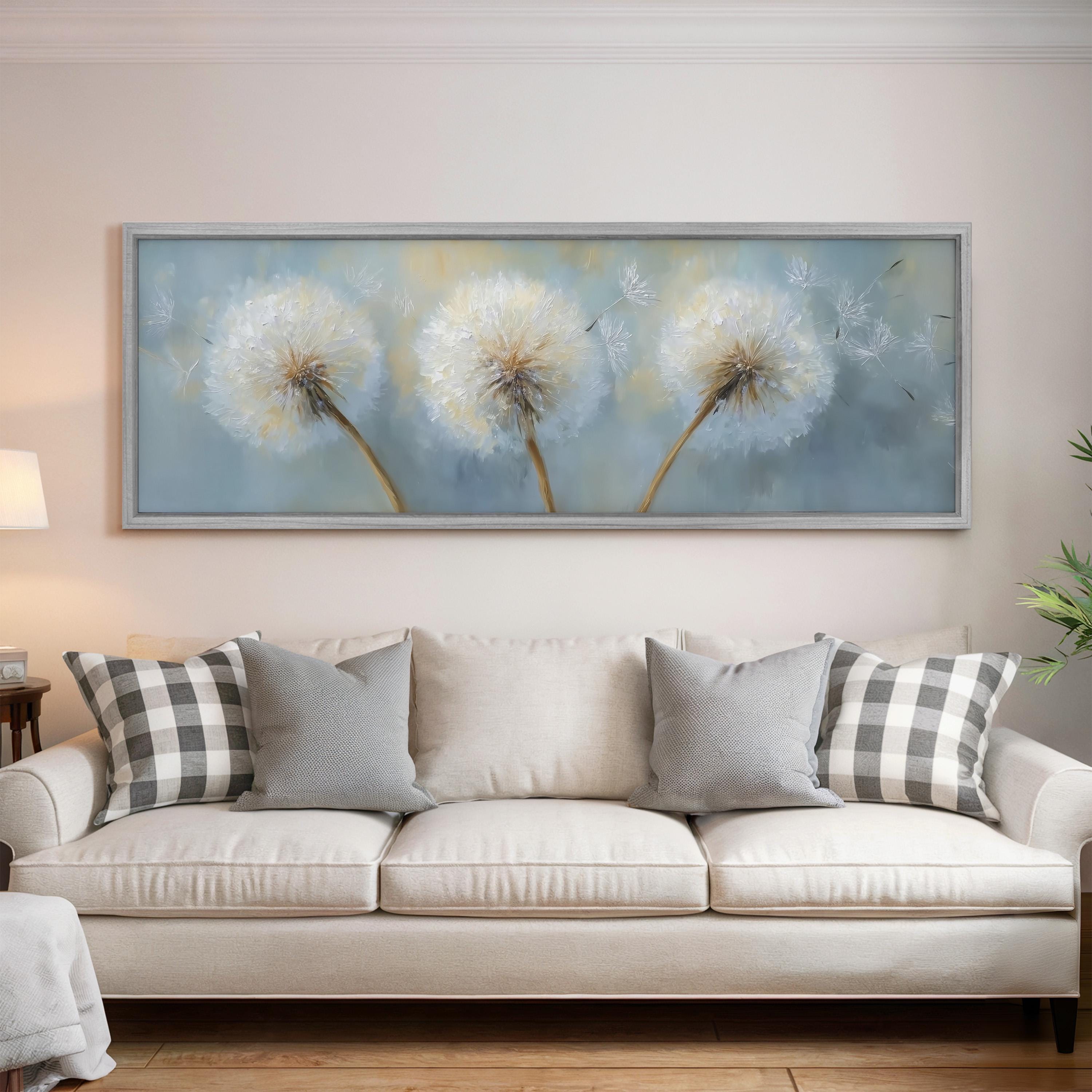a large framed painting of three dandelions hanging on a wall above a white sofa with gray and white plaid throw pillows.