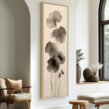 a minimalist living room with a large framed artwork of black and white flowers hanging on the wall. The room is furnished with a chair, a table, and a window with a plant on the sill.