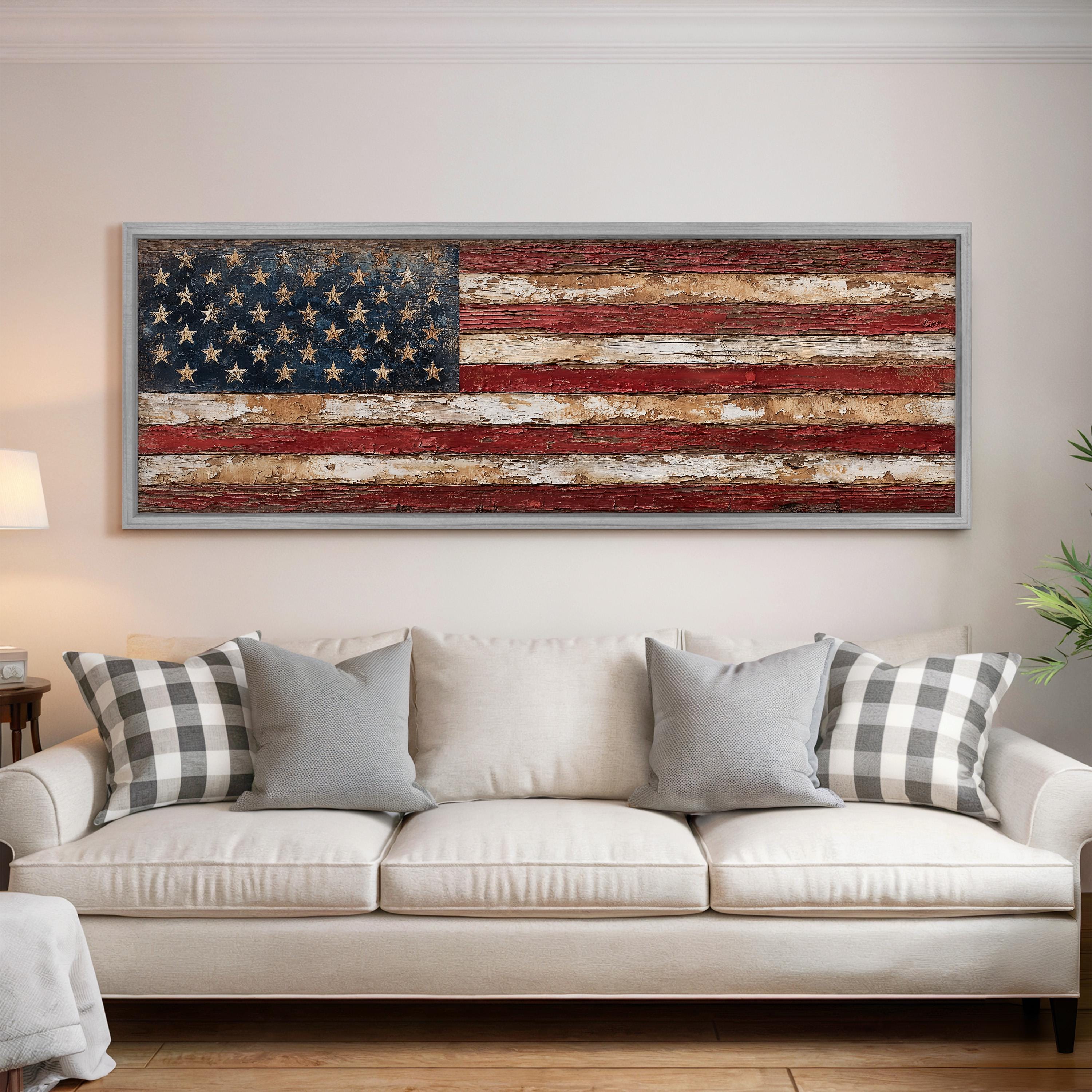 a large American flag displayed on the wall above a white couch with gray and white plaid throw pillows.