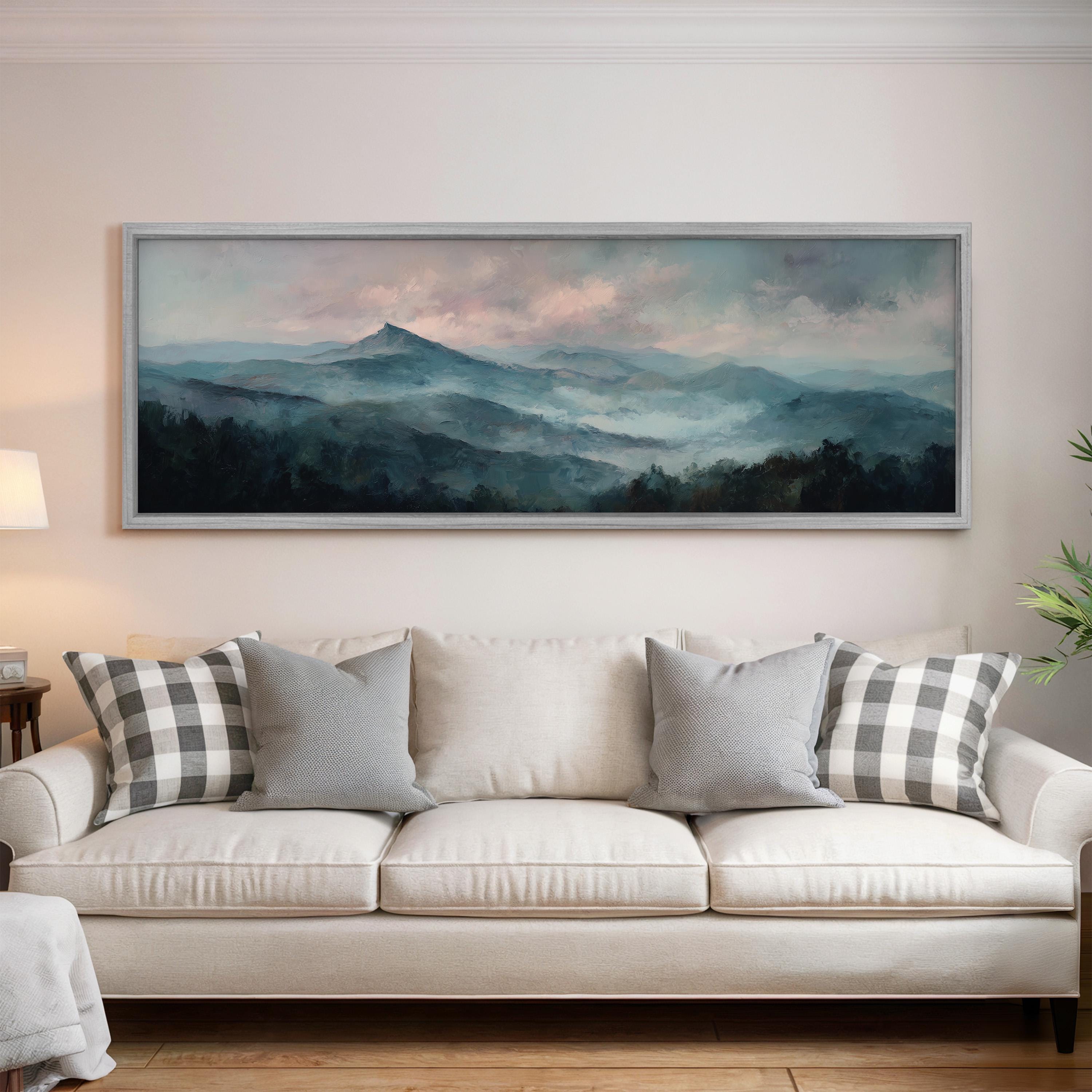 a large painting of a mountain landscape hanging on a wall above a white sofa with gray and white patterned pillows.