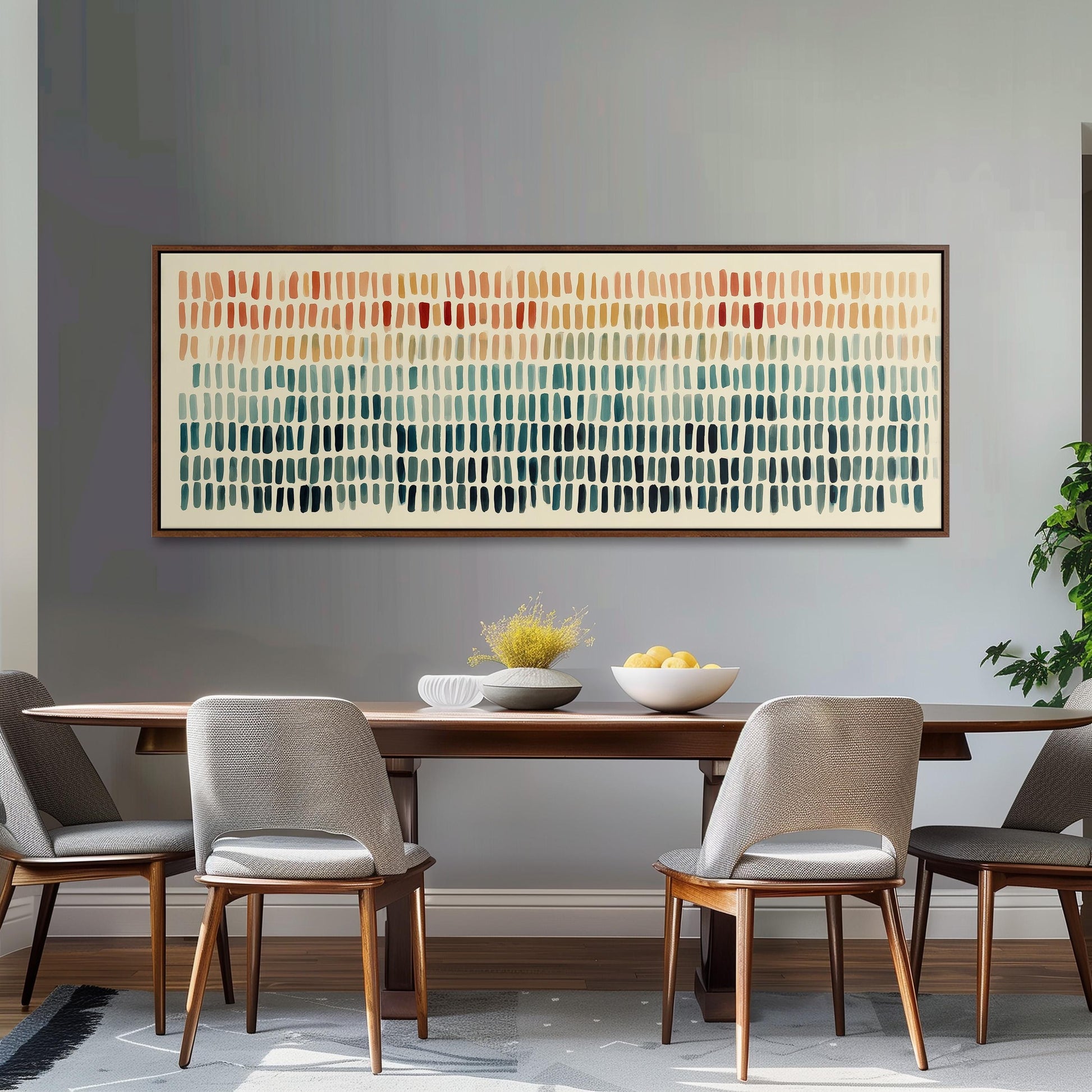 a dining room with a wooden table and four gray chairs. Above the table, there is a large abstract painting with a grid-like pattern in various shades of orange, green, and blue. The table is set with a bowl of fruit and a vase of flowers, creating a cozy and inviting atmosphere.