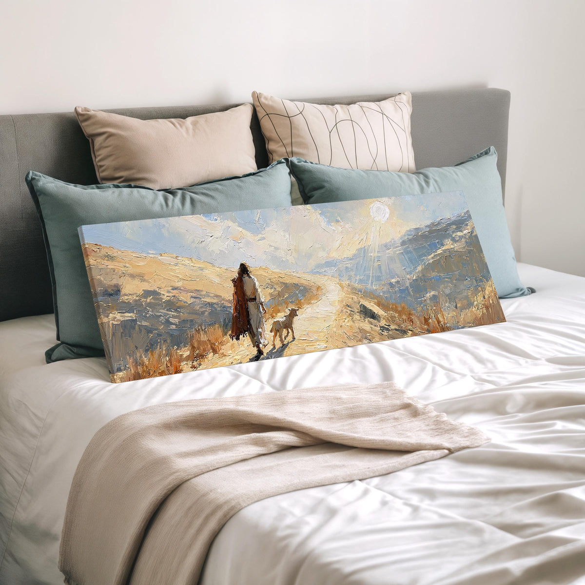Jesus walking a sunlit hillside path with a sheep wide panoramic canvas print laid on a bed to show its size