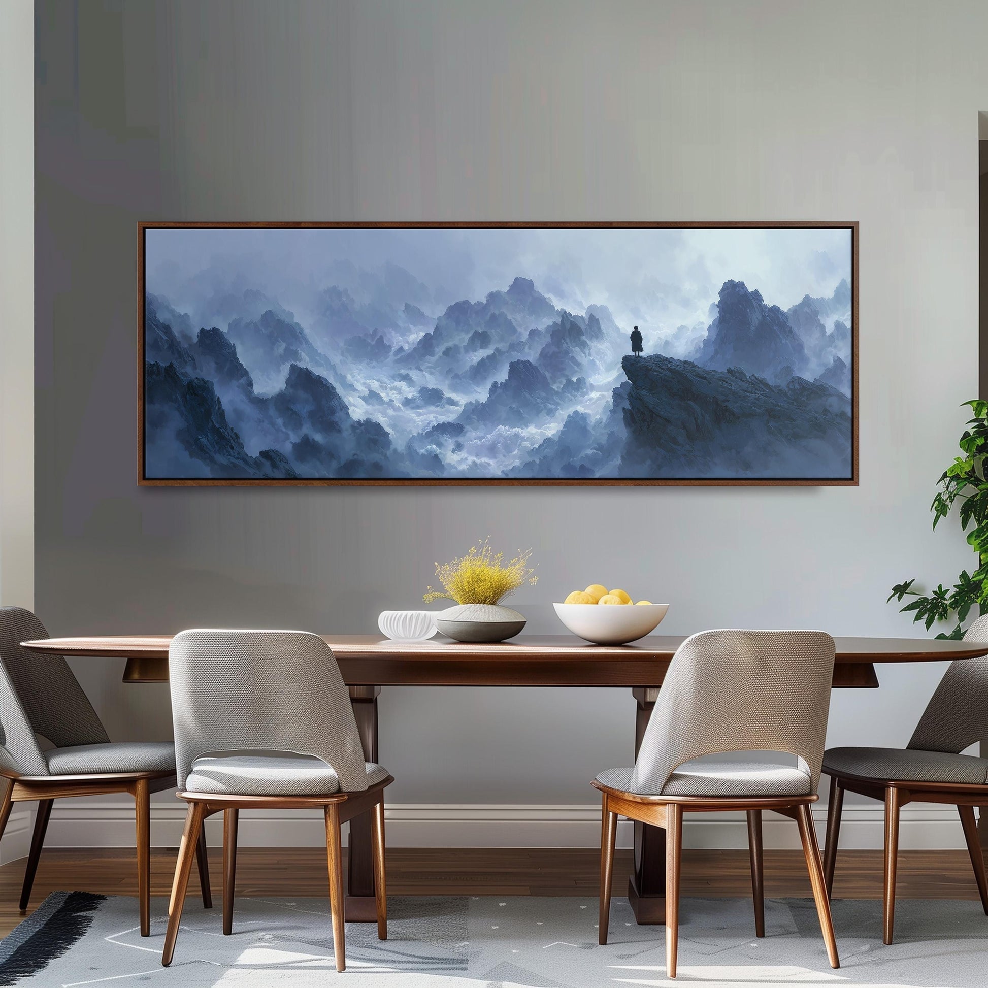 a large painting of a mountainous landscape hanging on a wall above a wooden dining table with four chairs. The painting depicts a person standing on a cliff overlooking the misty, mountainous terrain.