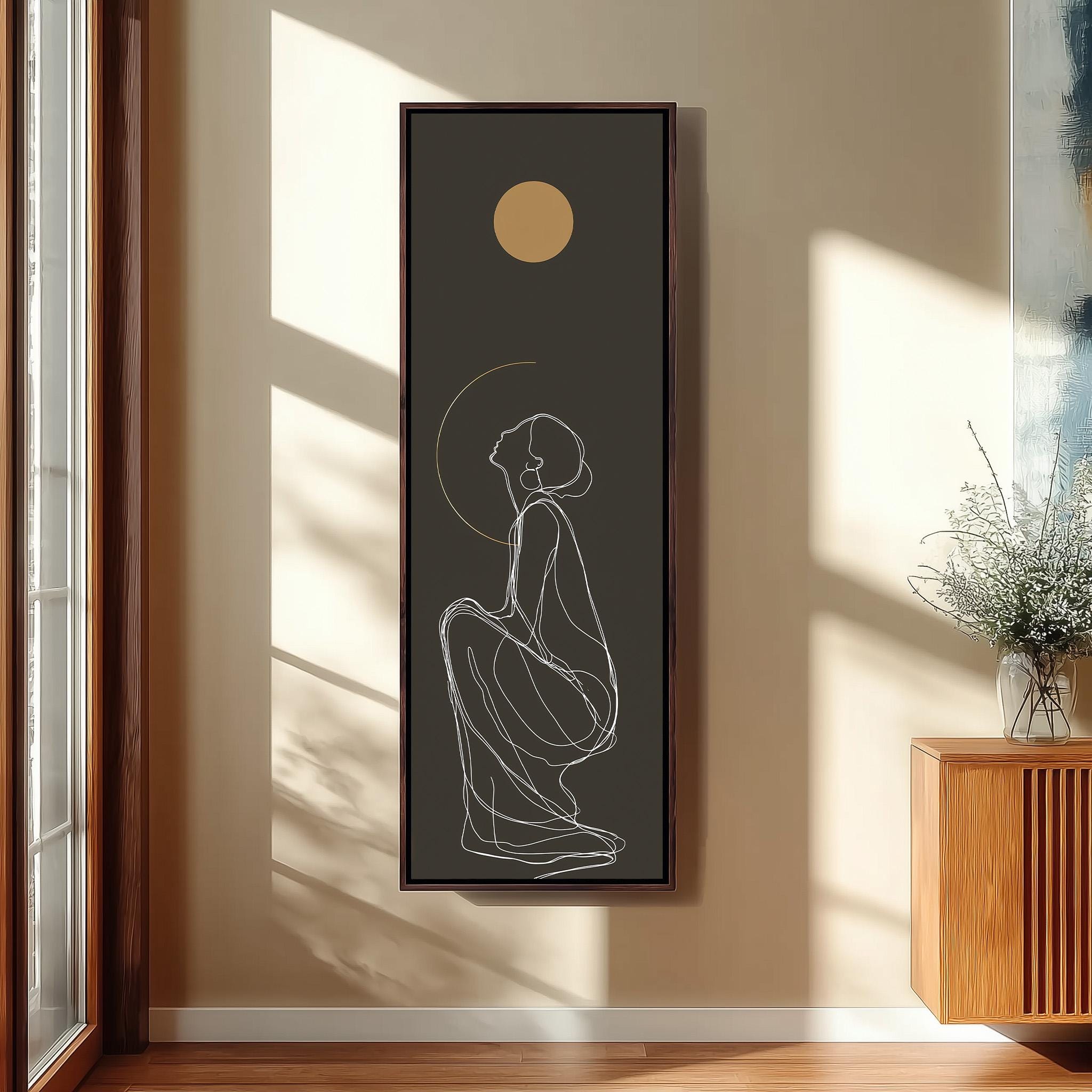 a framed artwork of a woman sitting on the floor, with a large sun or moon in the background.