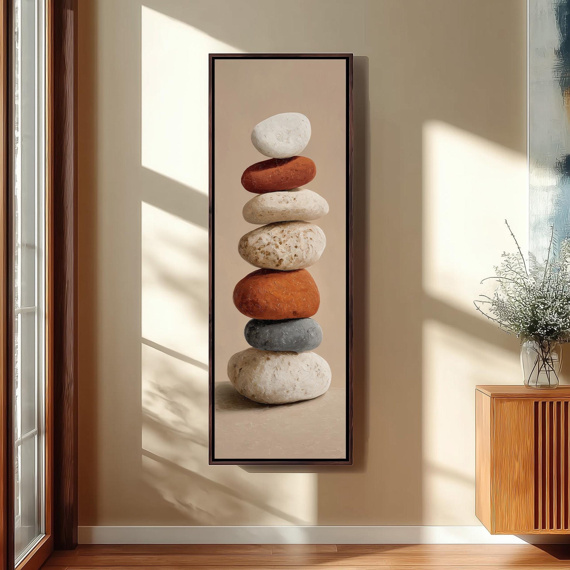 A framed photograph of a stack of rocks in various colors, including white, orange, and gray, is displayed on a wall in a room with a wooden cabinet and a vase of flowers.