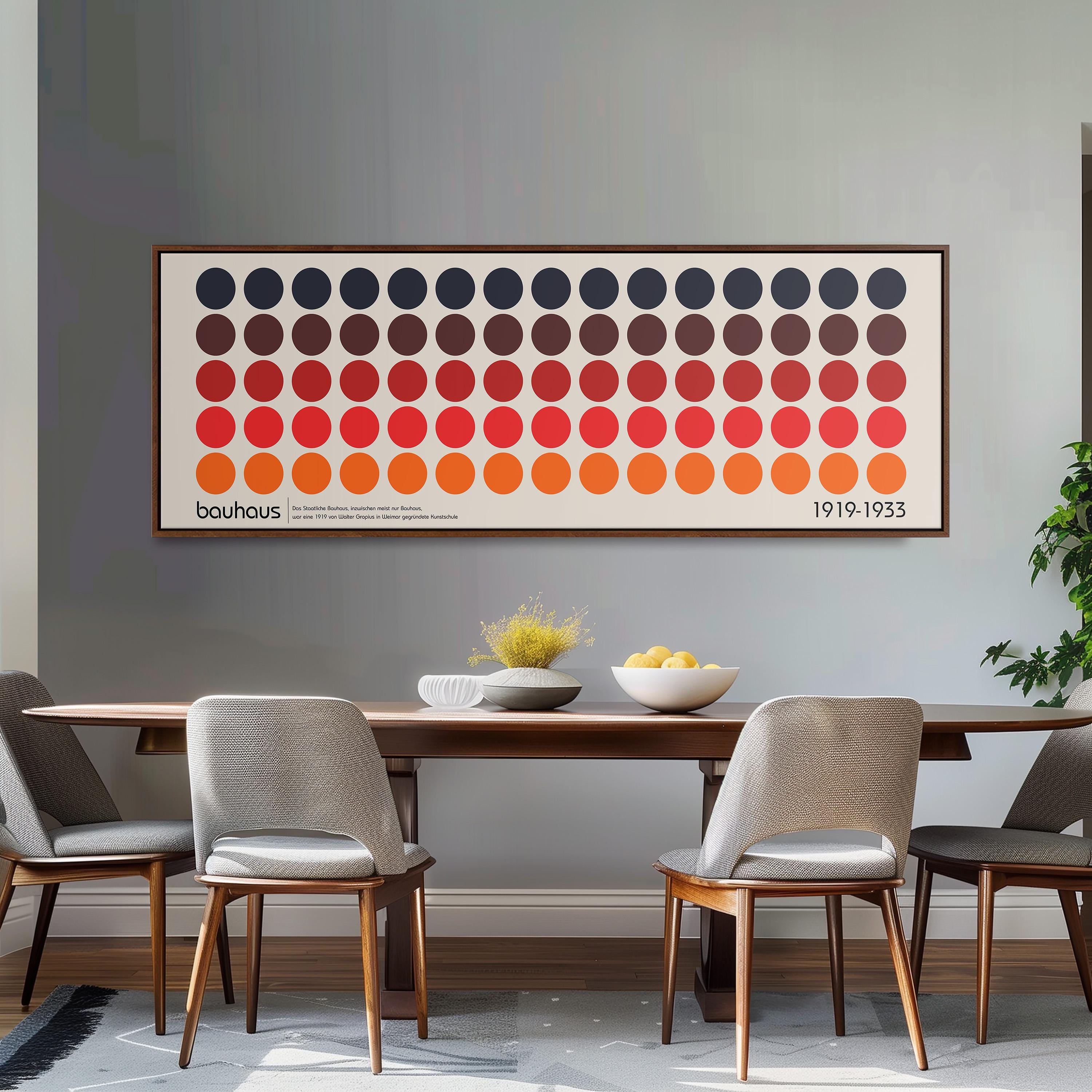 a dining room with a wooden table and four chairs. Above the table, there is a large framed poster with a repeating pattern of circles in various colors. The poster is hanging on a gray wall. On the table, there is a bowl of fruit and a vase of flowers.