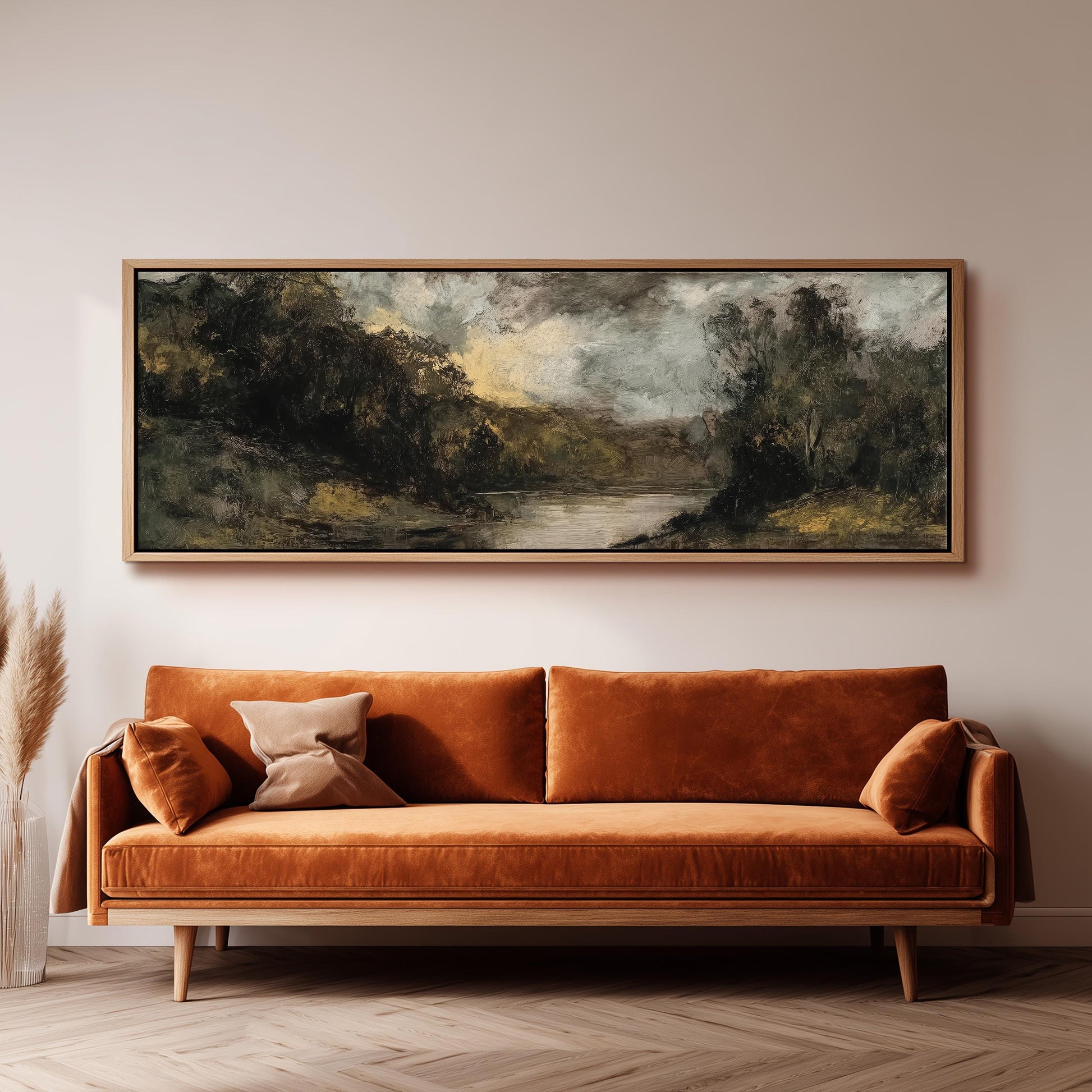 a large, framed landscape painting hanging on a wall above a brown sofa with orange cushions.
