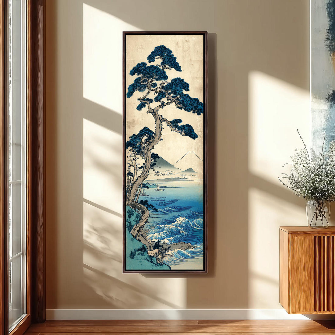 a large framed painting of a blue pine tree with a mountainous landscape in the background, hanging on a wall in a room with a wooden cabinet and a vase of flowers.