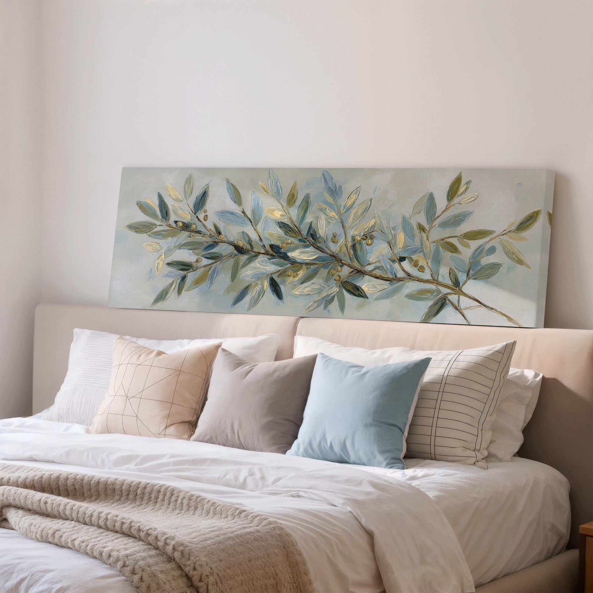 a large painting of a branch with green leaves and a blue background hanging above a bed with white sheets and pillows.