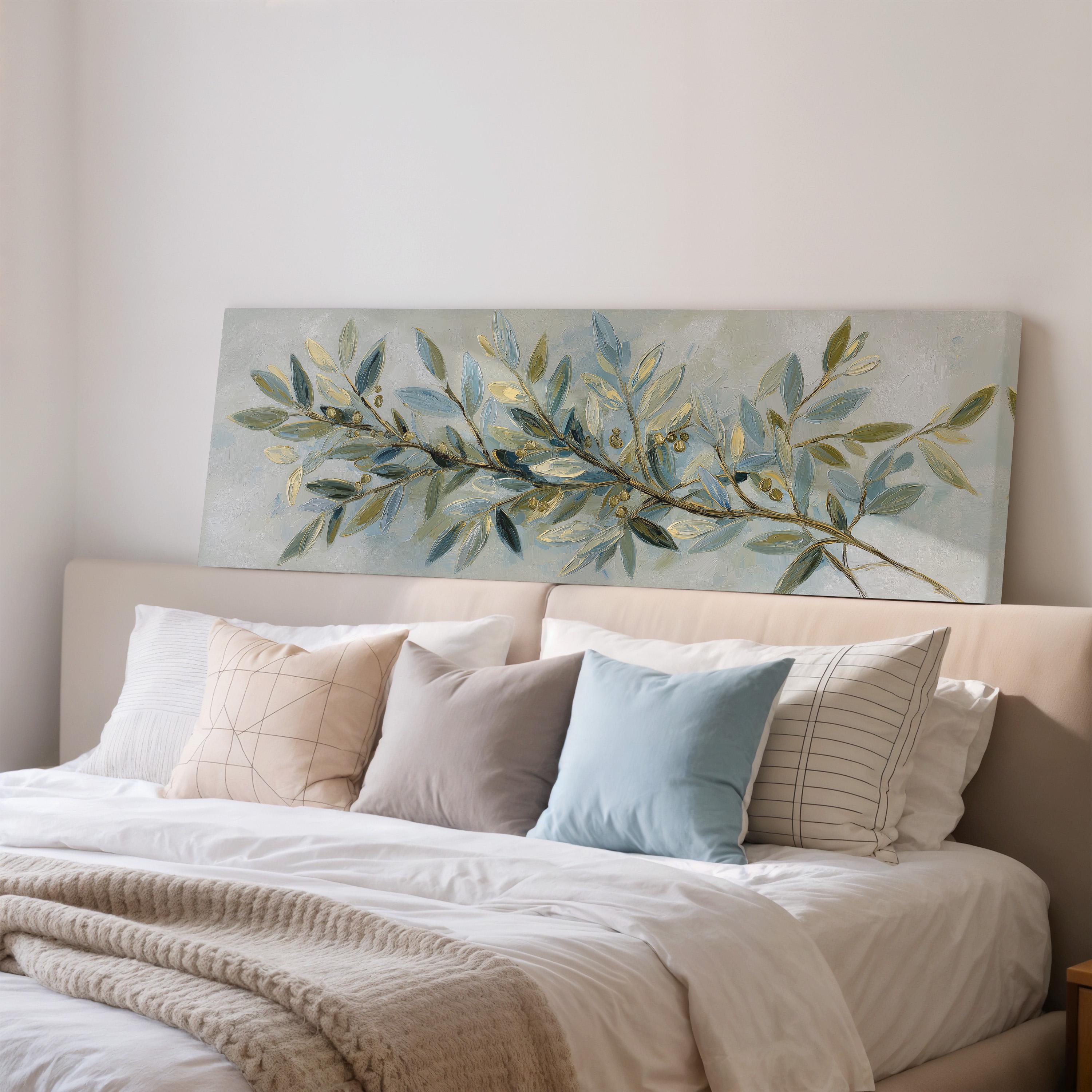 a large painting of a branch with green leaves and a blue background hanging above a bed with white sheets and pillows.
