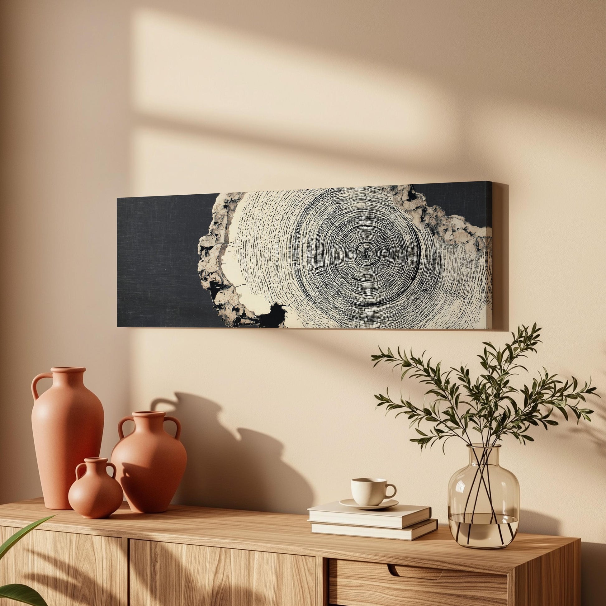 a wooden cabinet with a vase, a coffee cup, and a stack of books on top. Above the cabinet, there is a framed artwork depicting a tree trunk with concentric circles.