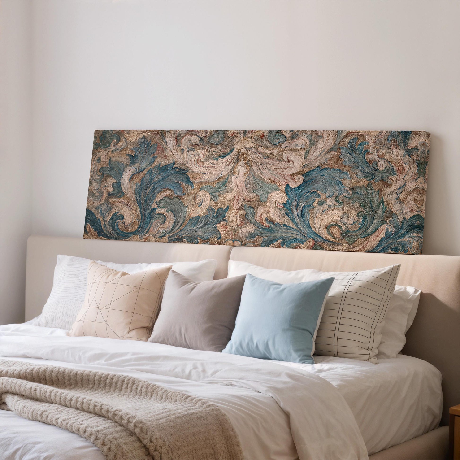 a well-made bed with a white comforter and several pillows, including a blue and white striped pillow, a gray and white striped pillow, and a beige and white striped pillow. Above the bed, there is a large painting or artwork with a floral pattern in shades of blue, green, and brown.