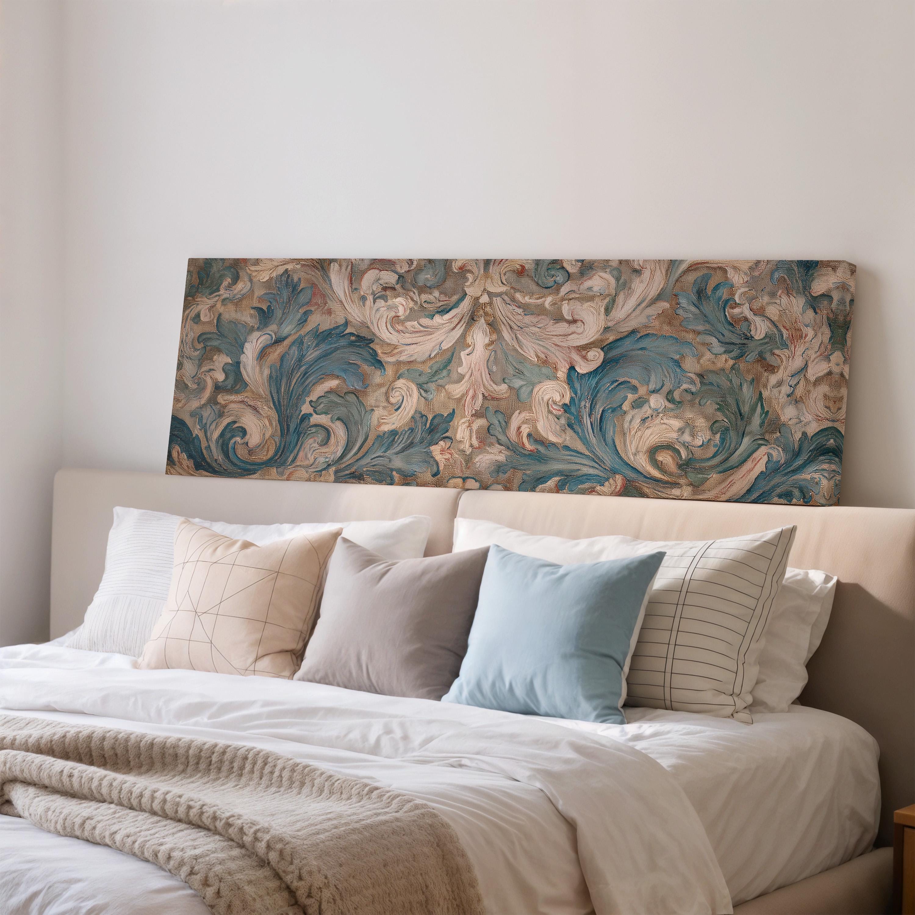 a well-made bed with a white comforter and several pillows, including a blue and white striped pillow, a gray and white striped pillow, and a beige and white striped pillow. Above the bed, there is a large painting or artwork with a floral pattern in shades of blue, green, and brown.