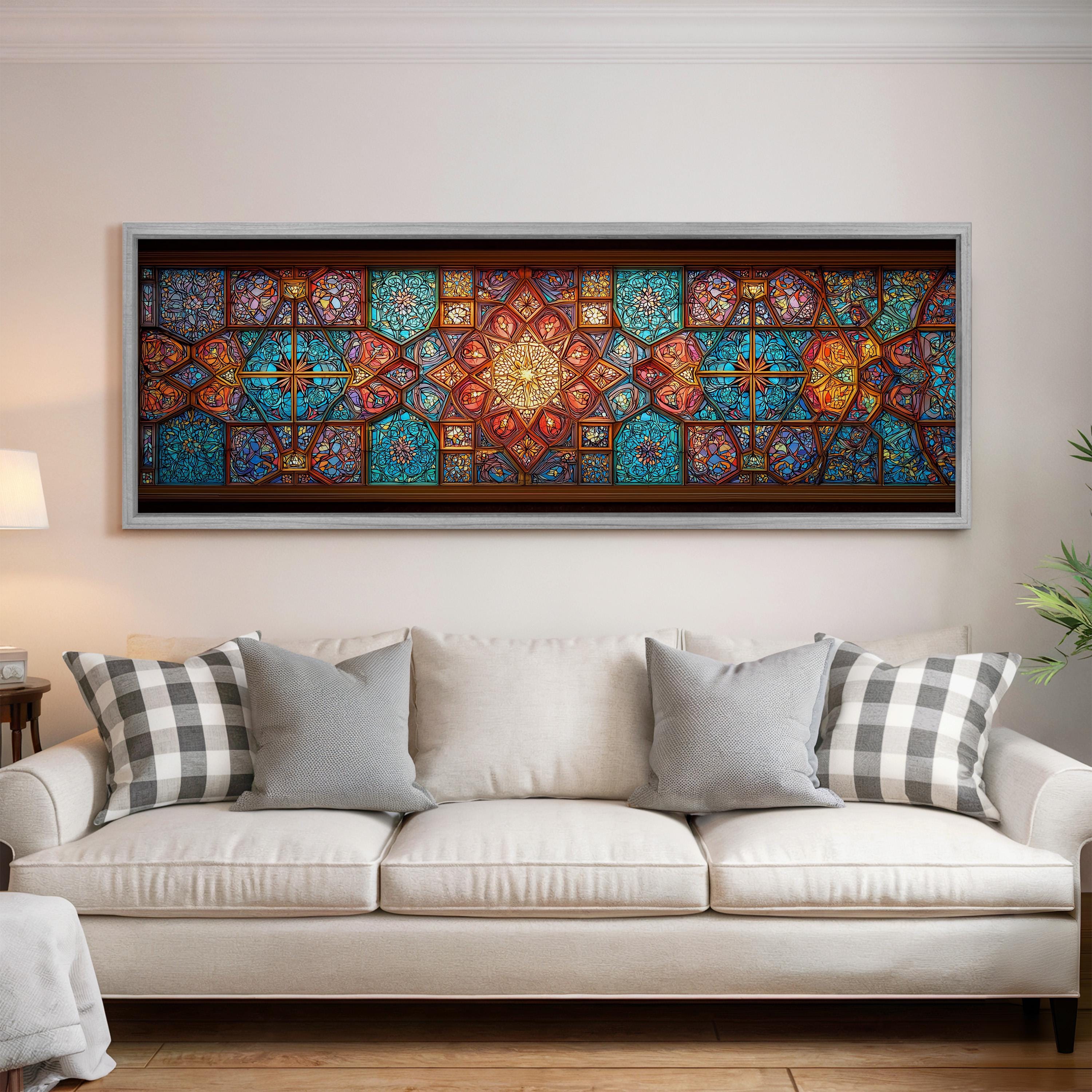 a large, colorful stained glass window with intricate patterns and designs, hanging on a wall above a white couch with gray and white plaid throw pillows.