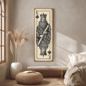 a large framed artwork depicting a king, a symbol often associated with power and authority. The king is shown in a standing position, wearing a crown and holding a scepter. The artwork is displayed on a wall in a room with a bed, a potted plant, and a woven ottoman.