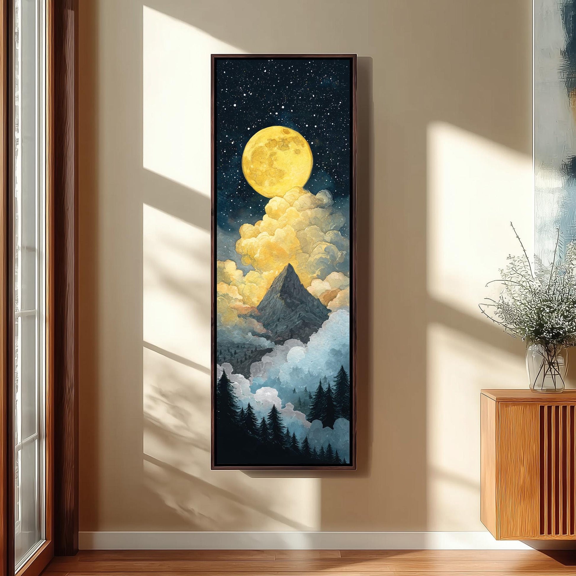 a large framed painting hanging on a wall, depicting a mountain landscape with a bright yellow moon and clouds in the night sky.