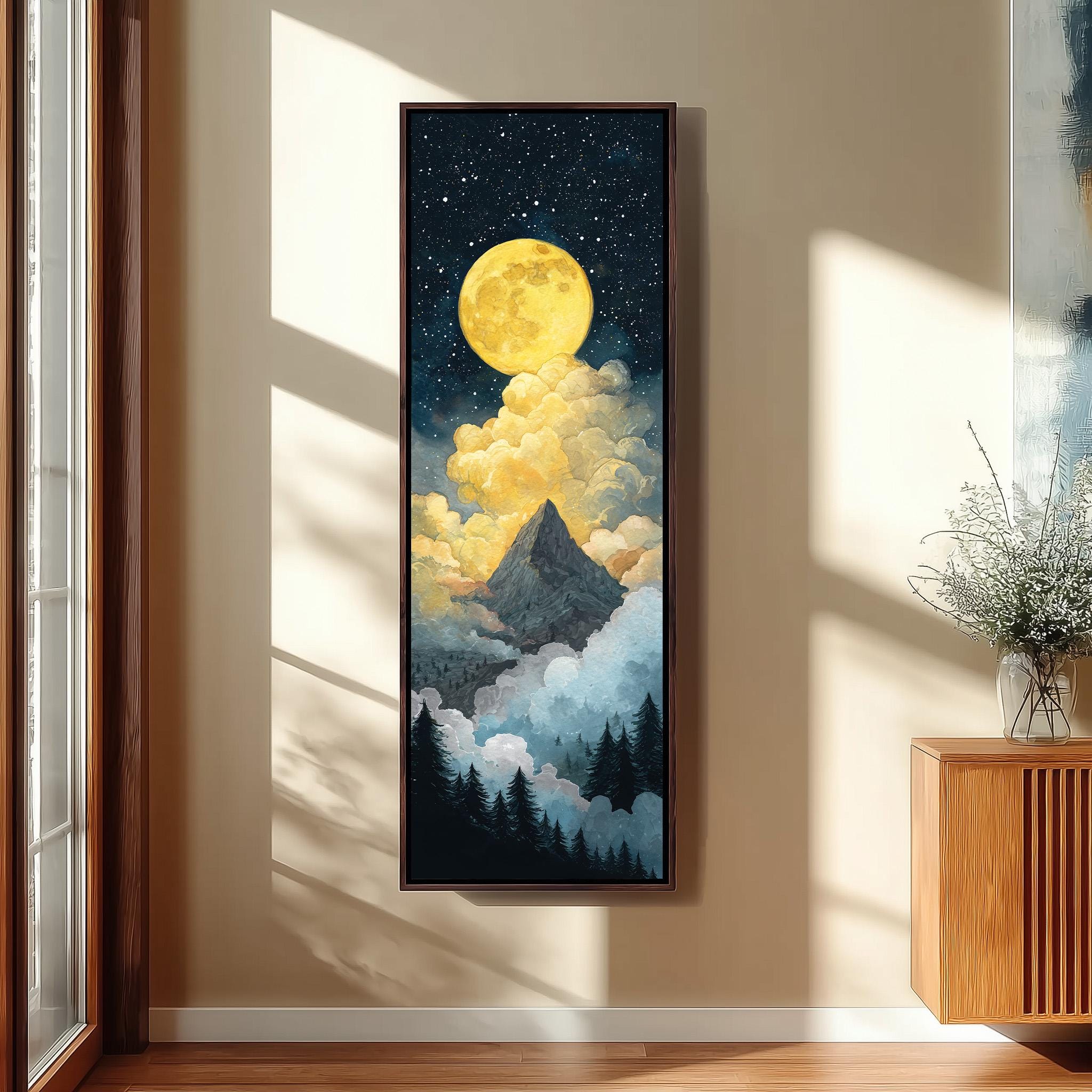 a large framed painting hanging on a wall, depicting a mountain landscape with a bright yellow moon and clouds in the night sky.