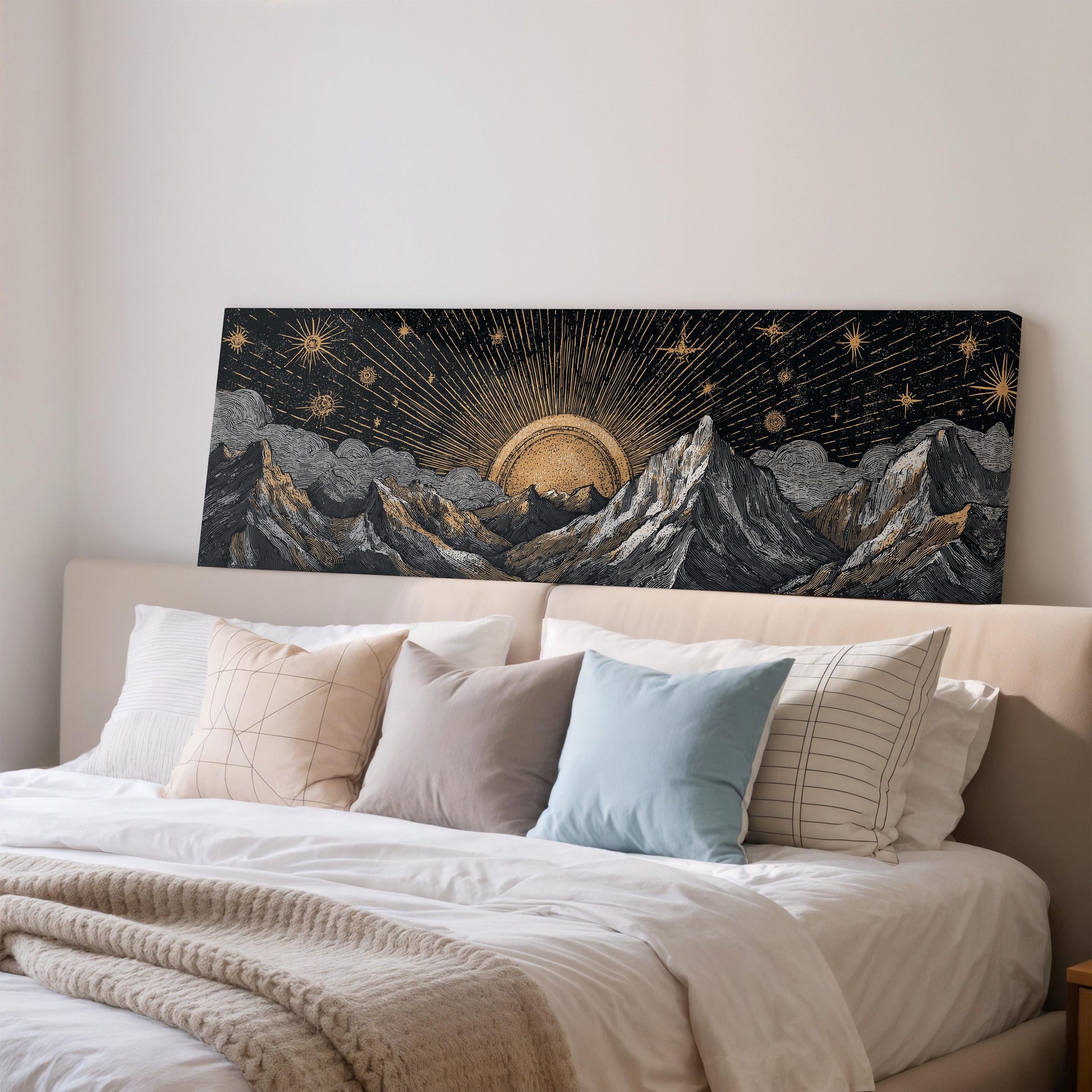 a large black canvas with a gold sun and mountains in the background, hanging above a bed with white pillows and a beige blanket.