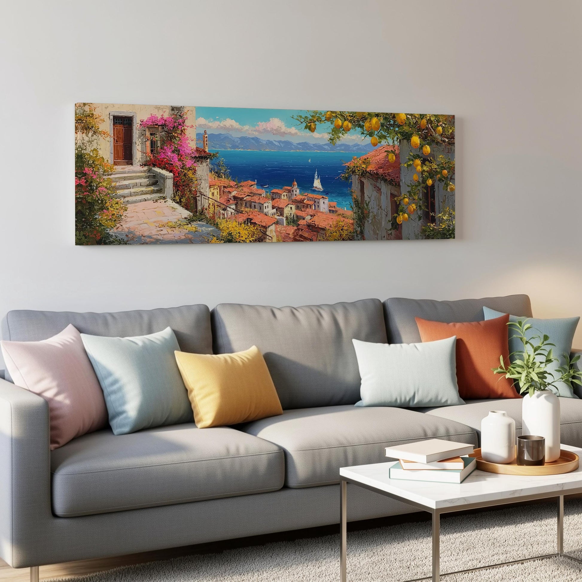 a large, colorful painting of a coastal town with a view of the ocean, hanging on a wall above a gray couch with colorful throw pillows.