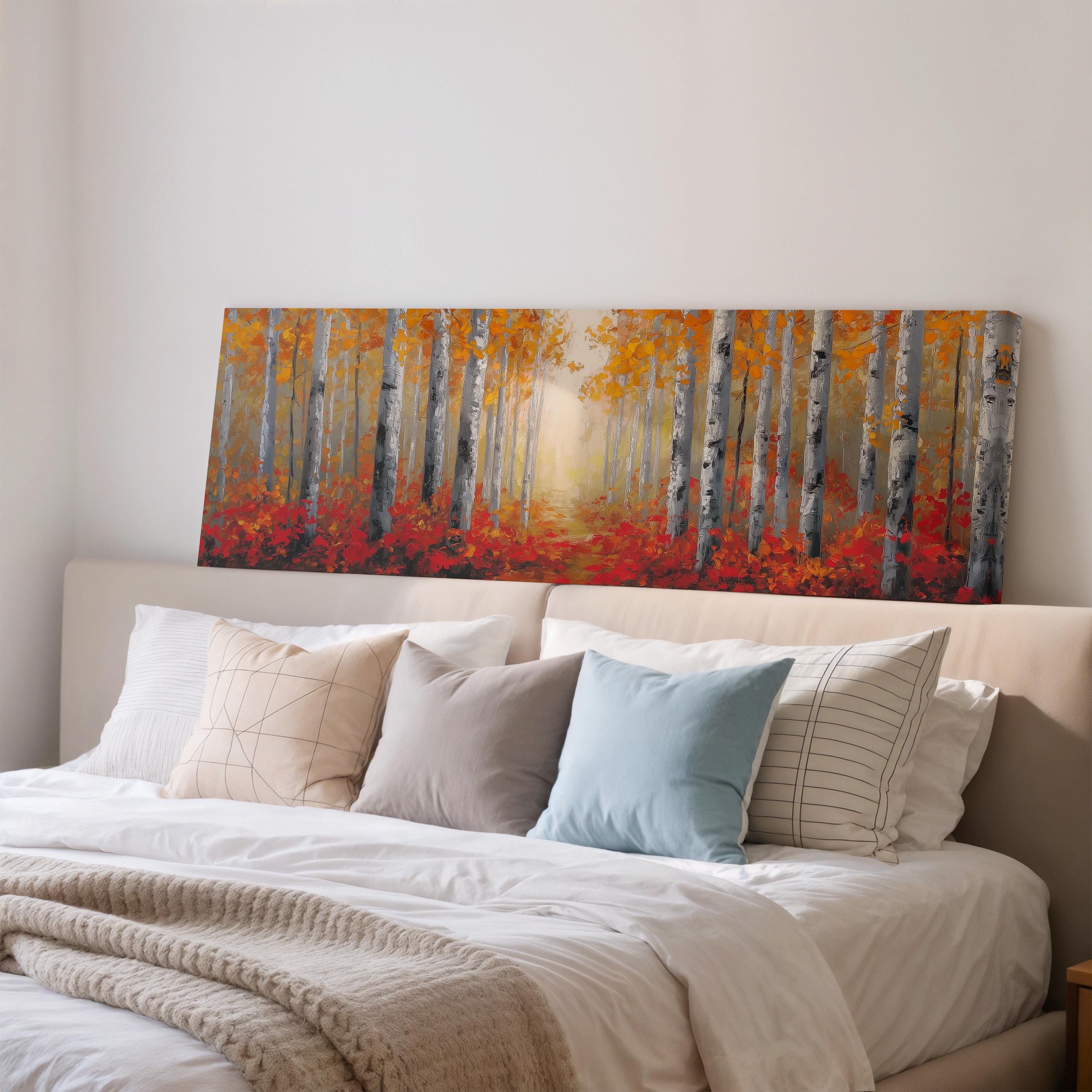 a large painting of a forest scene with tall trees and red leaves, hanging above a bed with white pillows and a gray blanket.