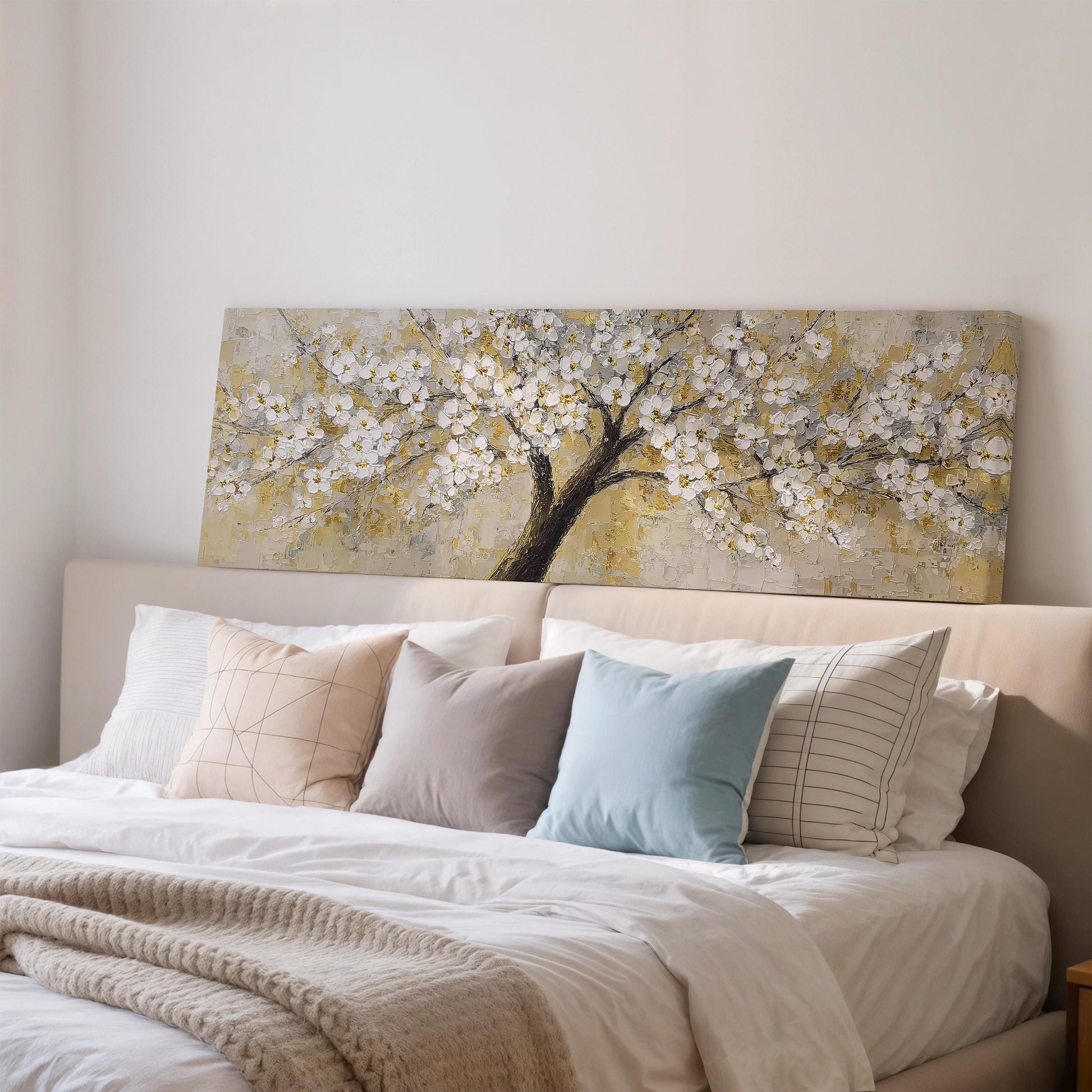 a large painting of a tree with white flowers hanging above a bed with white sheets and pillows.