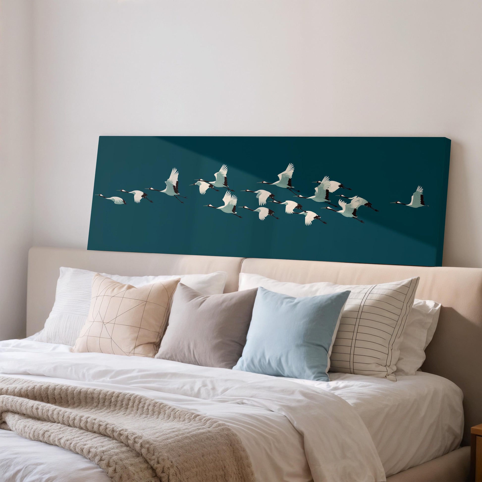 a large canvas print of a flock of white birds flying over a dark blue background, mounted on a wall above a bed with white pillows and a gray blanket.