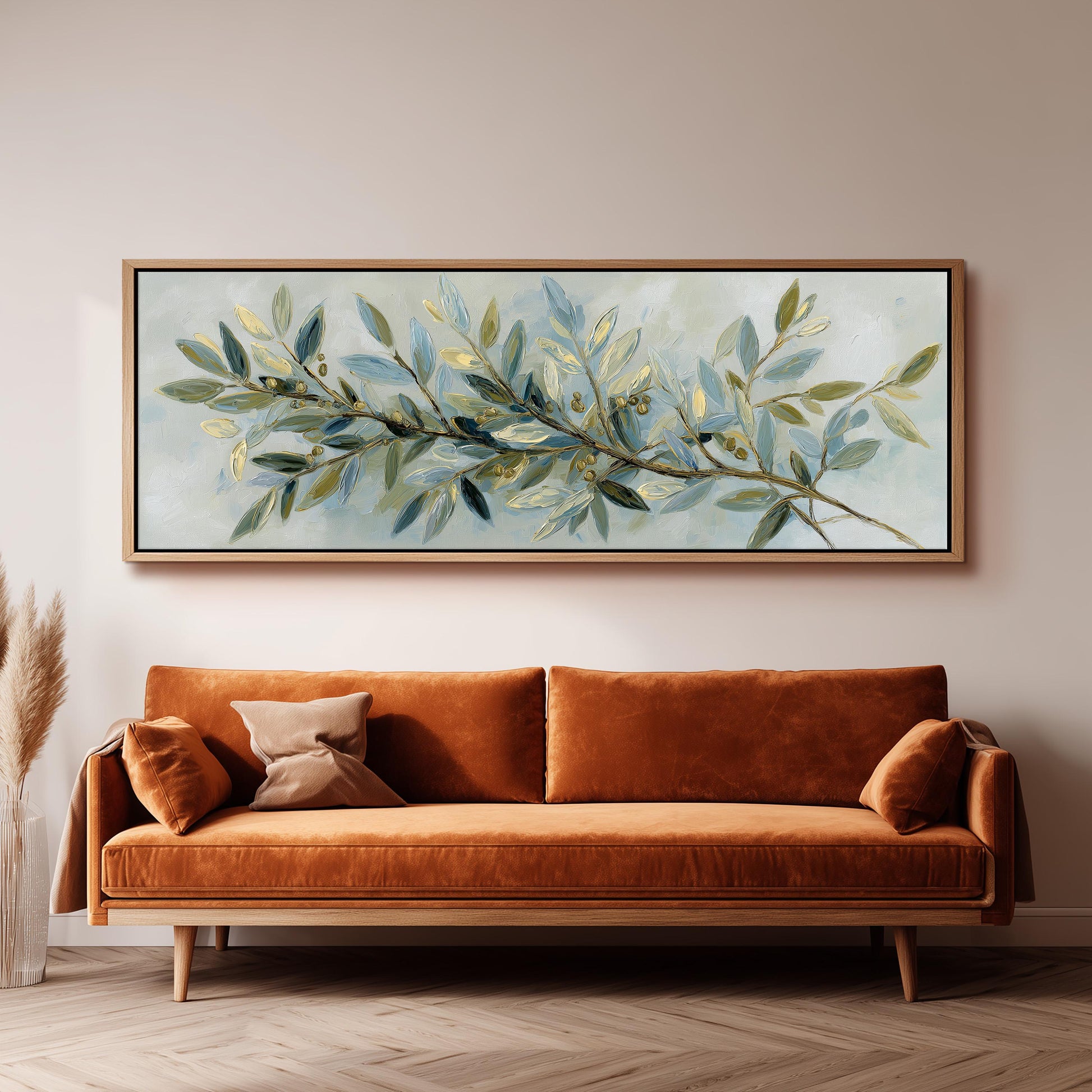 a large painting of a branch with green leaves hanging on a wall above a brown sofa.