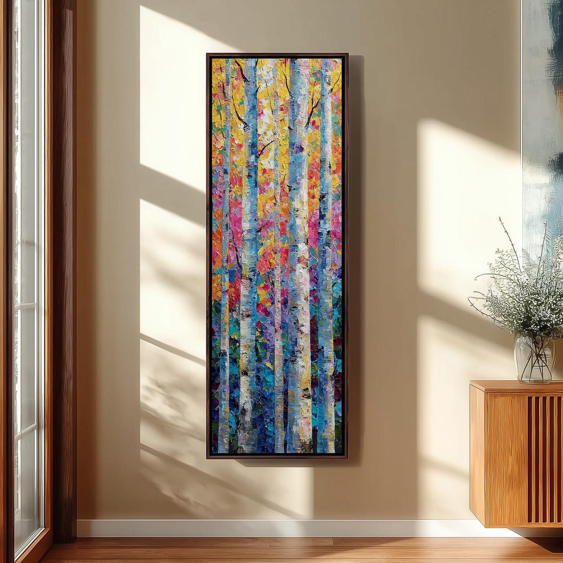 a large, colorful painting of trees hanging on a wall in a room with a wooden floor and a window.