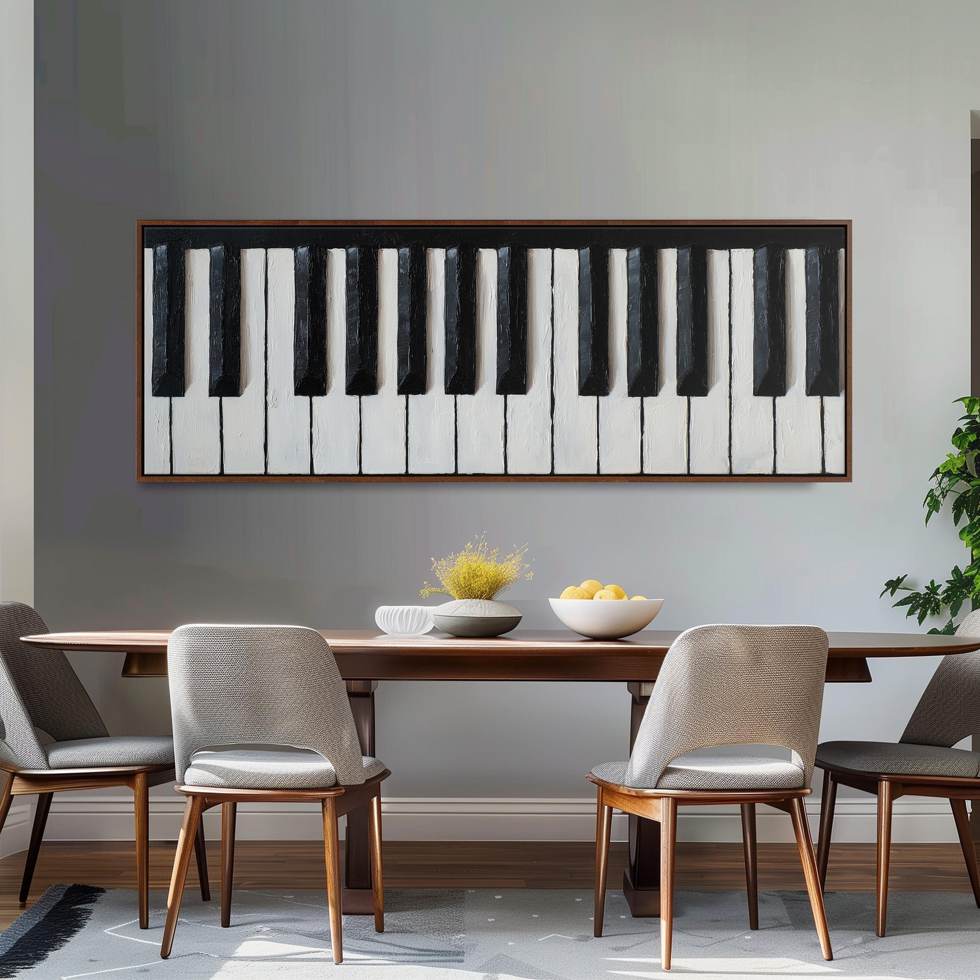 a dining room with a wooden table and four chairs. Above the table, there is a large black and white piano keyboard painting on the wall. On the table, there is a bowl of fruit and a vase of flowers.