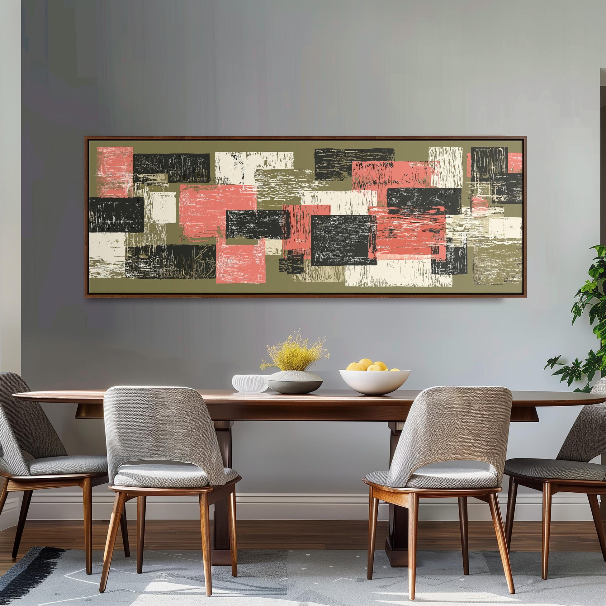 a dining room with a wooden table and four chairs. Above the table, there is a large abstract painting with a mix of pink, green, and black colors. The painting is hanging on a gray wall, and the dining table is set with a bowl of fruit and a vase of flowers.