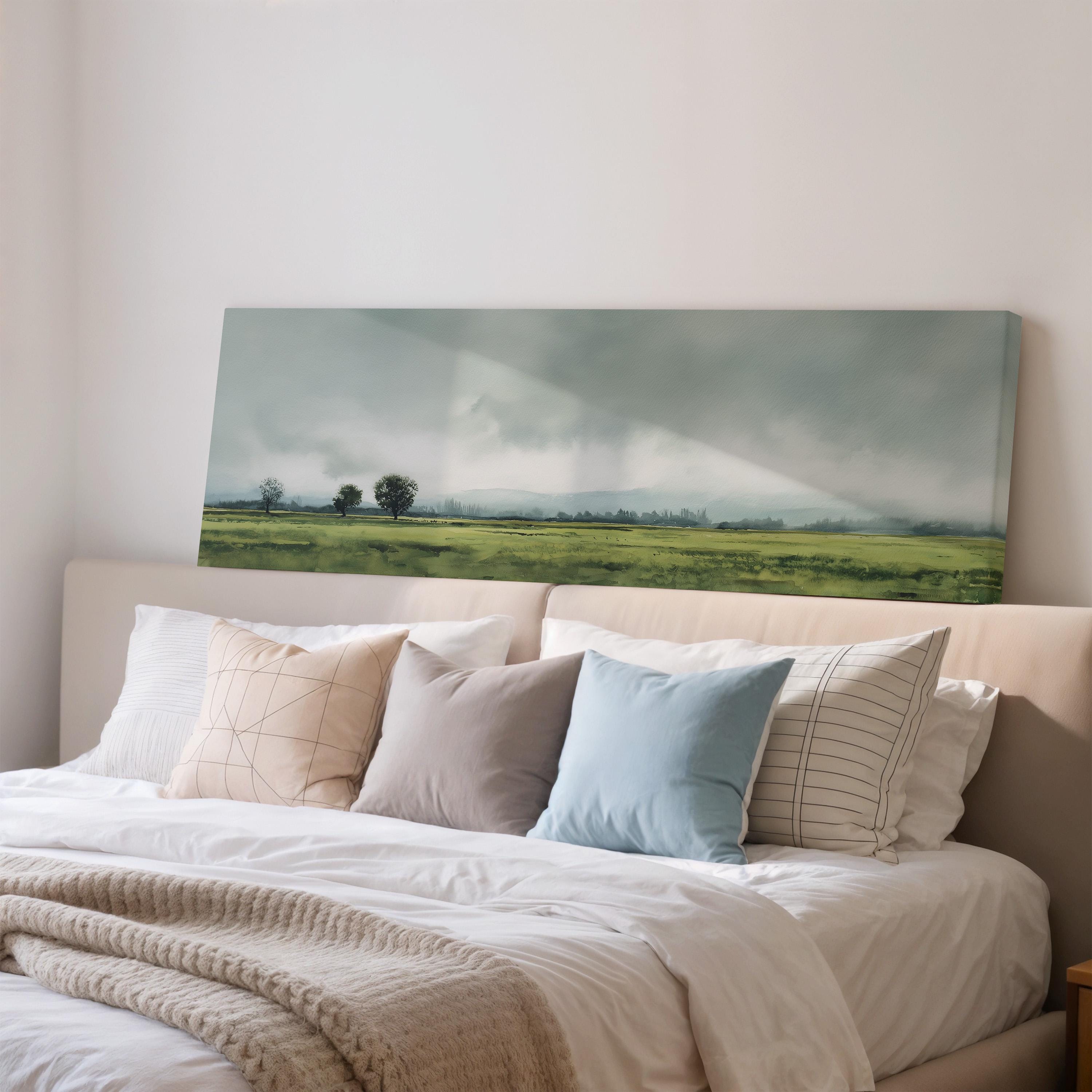 a large landscape painting hanging on a wall above a bed with white pillows and a gray blanket.