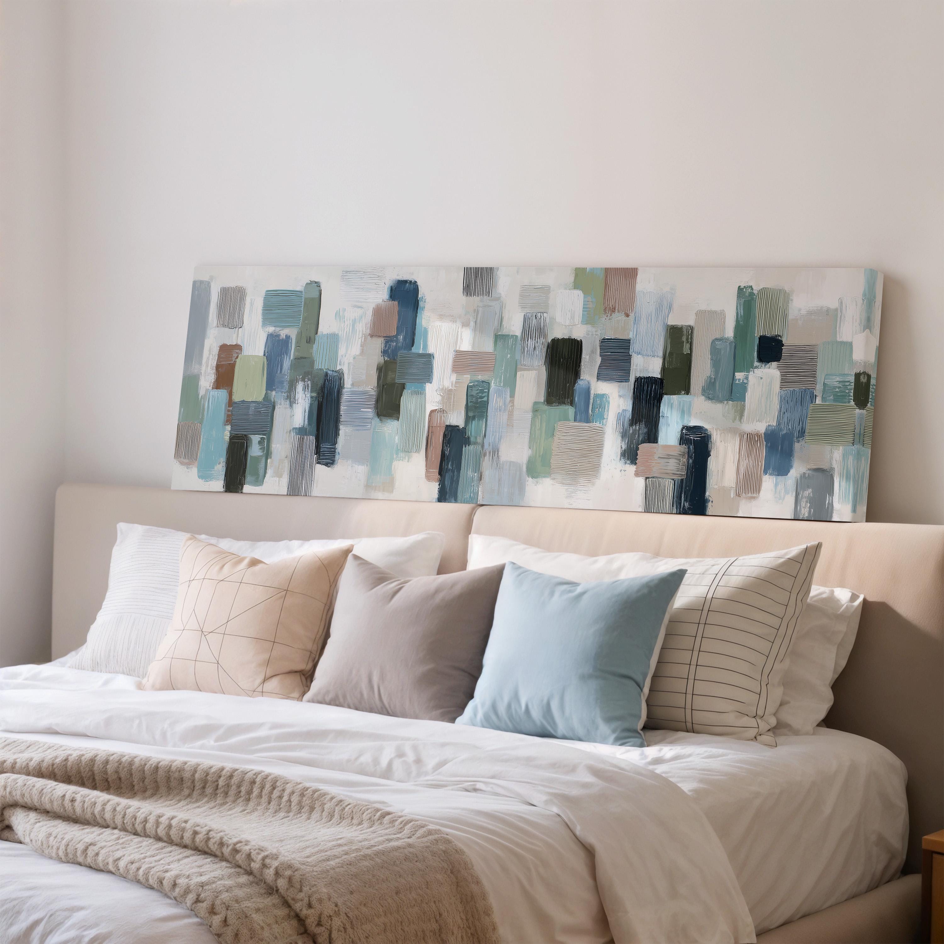 a well-made bed with a white comforter and several pillows in various colors and patterns. Above the bed, there is a large abstract painting or artwork on the wall.
