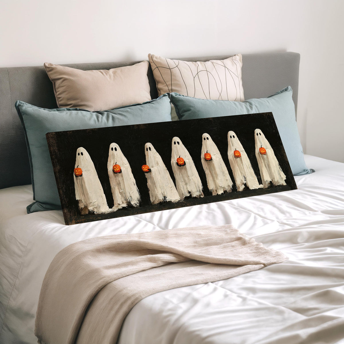 Row of ghosts holding pumpkins wide panoramic canvas print laid on a bed to show its size