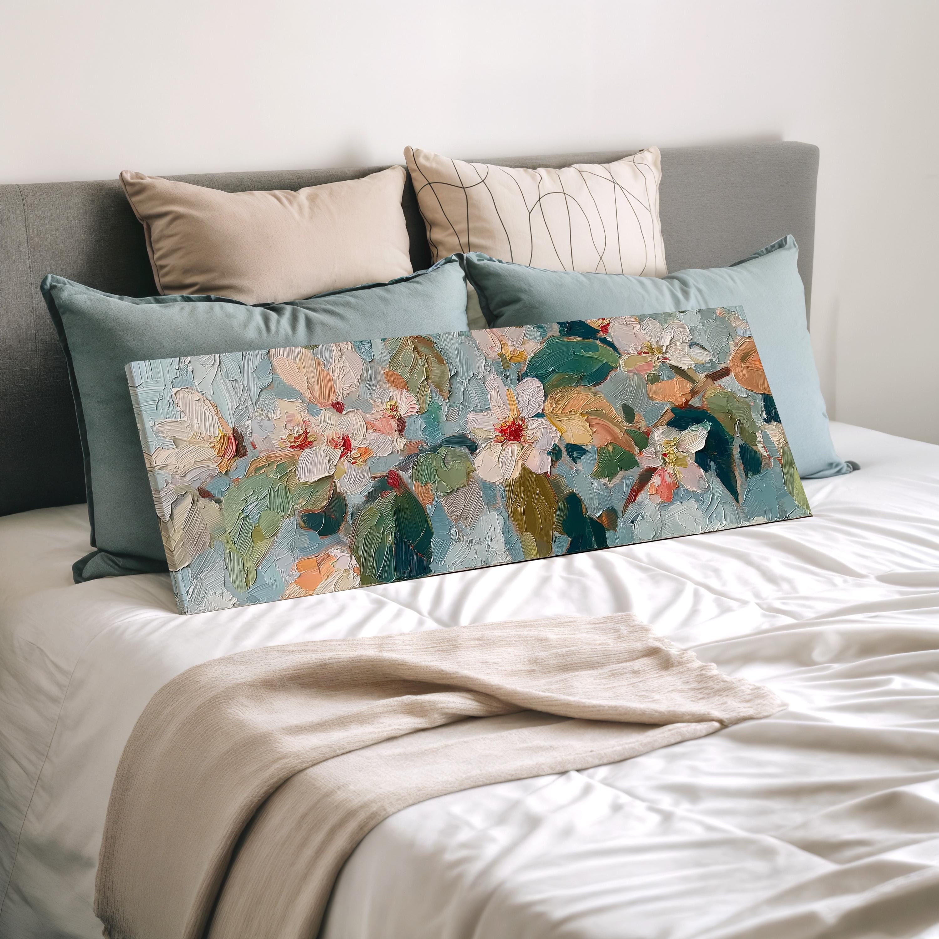 a bedroom with a bed covered in white sheets and a large floral painting resting on the bed. The painting features a variety of colorful flowers and leaves, creating a vibrant and lively atmosphere.