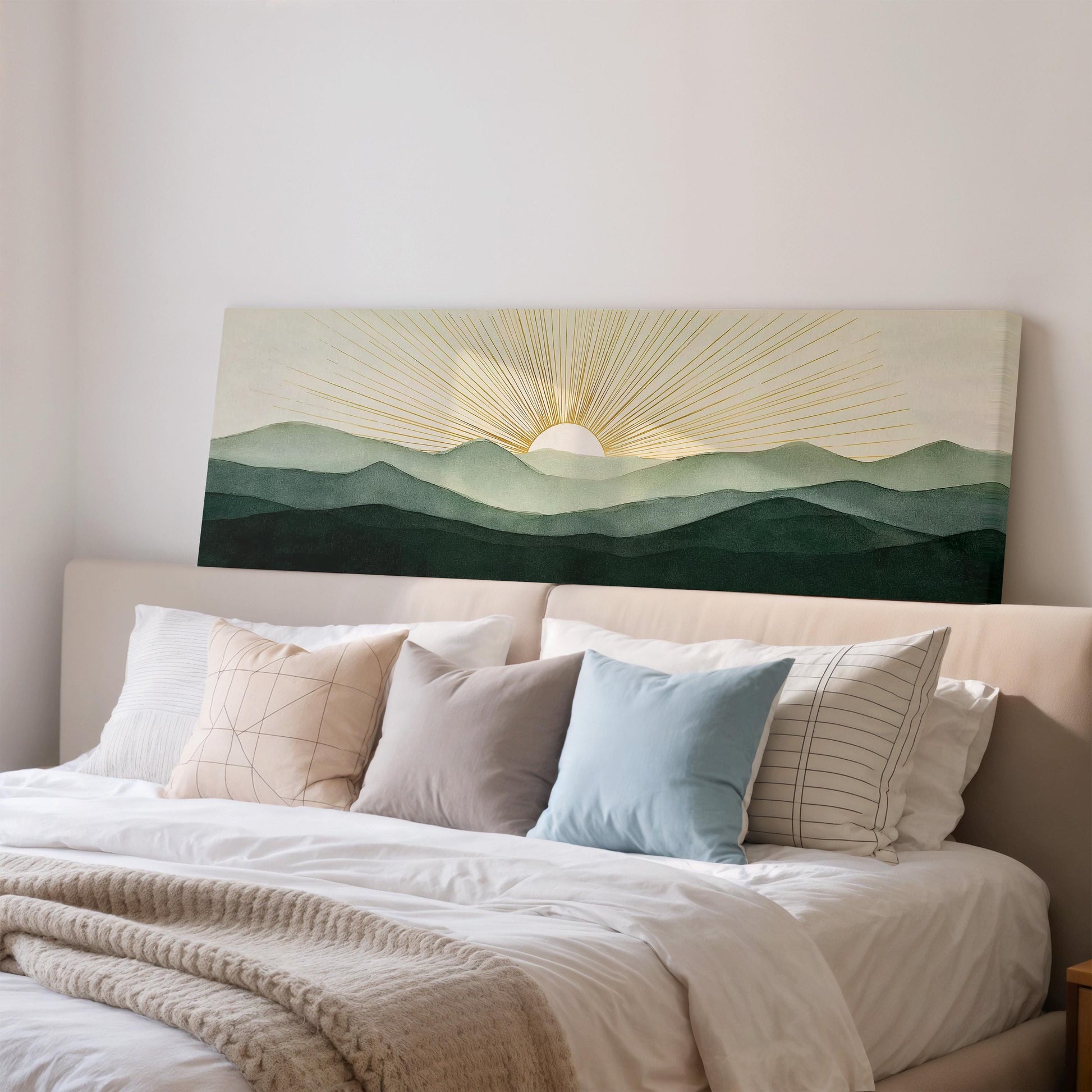 a large bed with a white comforter and a variety of pillows, including a blue pillow and a striped pillow. Above the bed, there is a large canvas print depicting a sunrise over a mountain landscape.