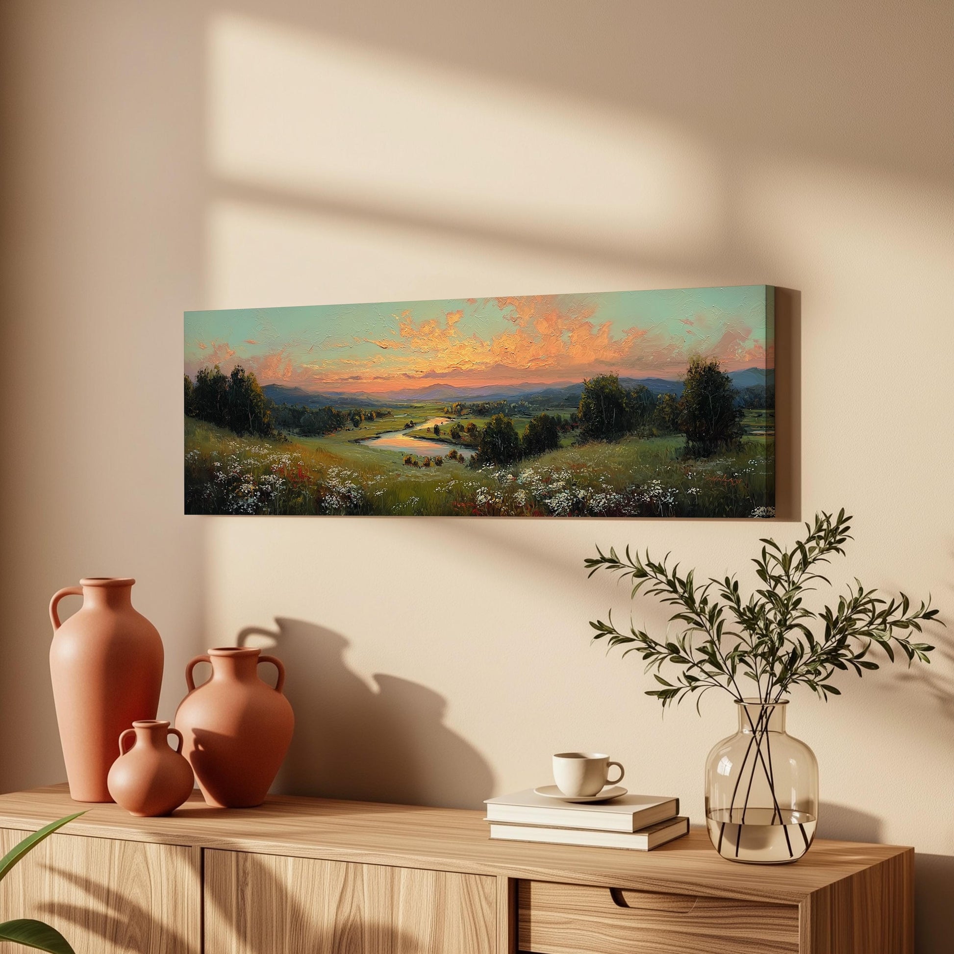 a wooden cabinet with a vase of greenery, a stack of books, and a painting of a landscape on the wall.