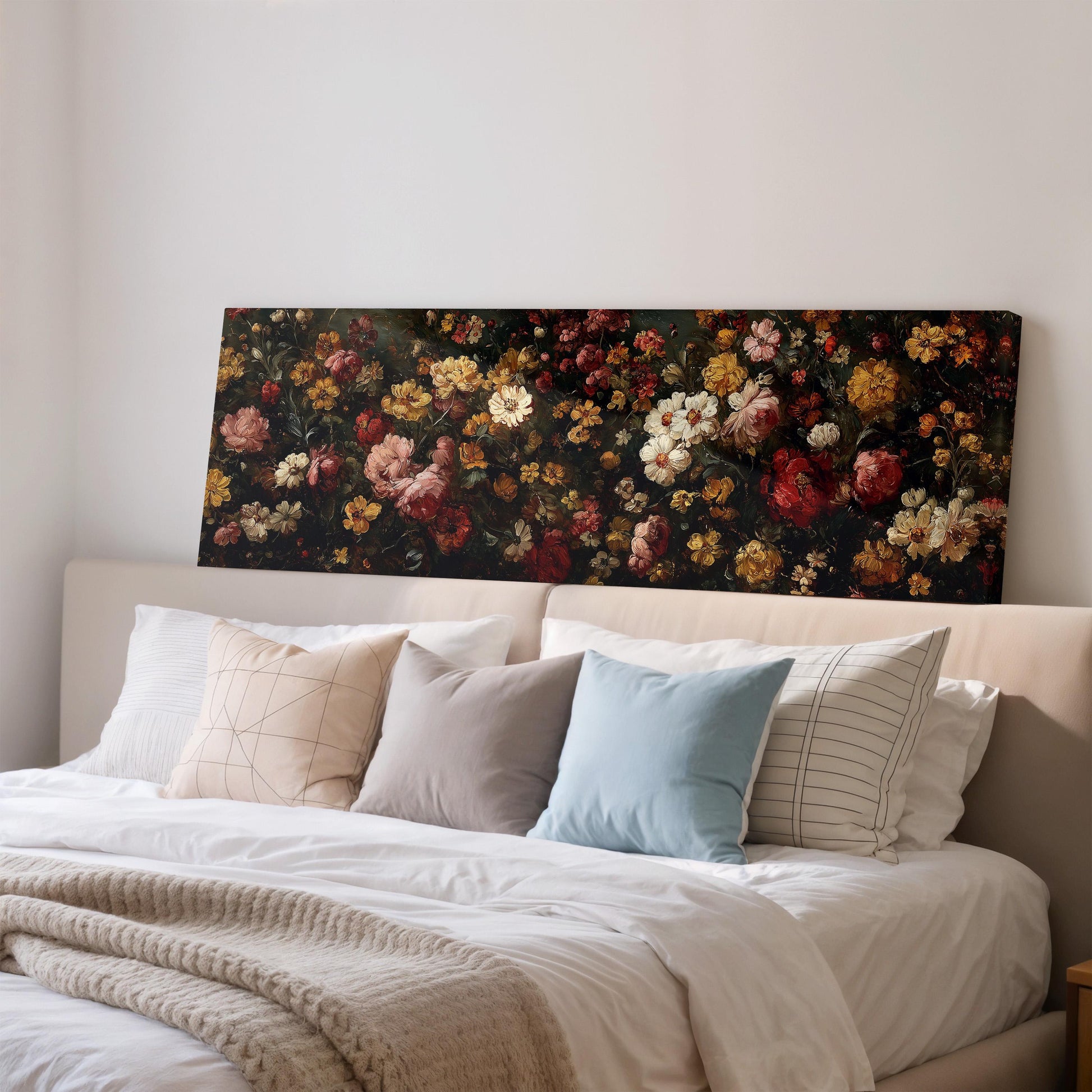 a large floral painting hanging on a wall above a bed with white pillows and a gray blanket.
