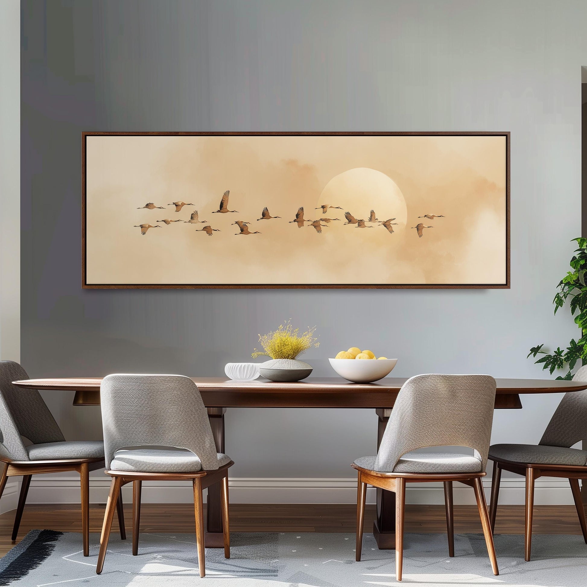 a dining room with a large painting of a flock of birds flying across a cloudy sky above a wooden table. The table is set with a bowl of fruit and a vase of flowers, creating a cozy and inviting atmosphere.