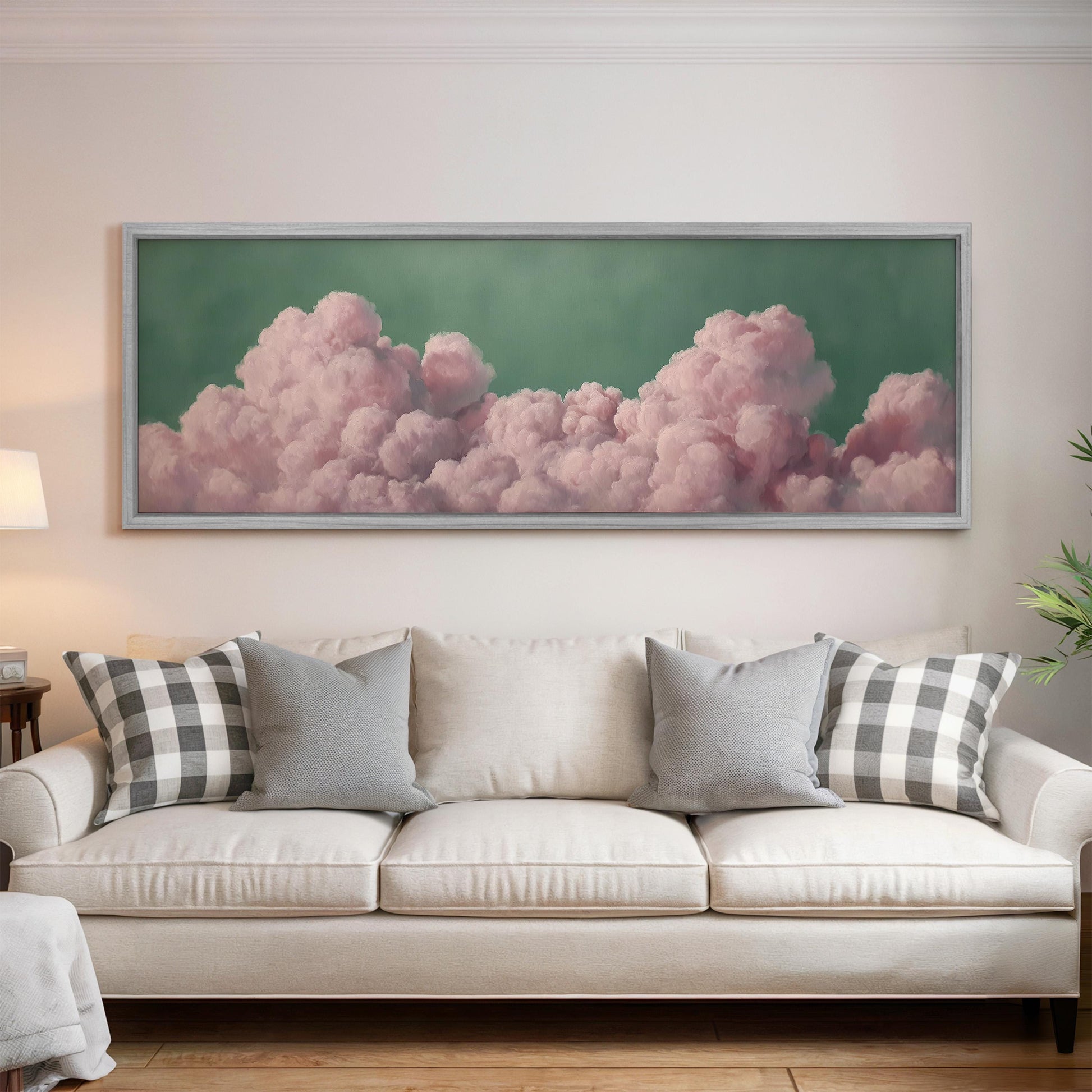 a large framed painting of pink clouds hanging on a wall above a white couch with gray and black plaid throw pillows.