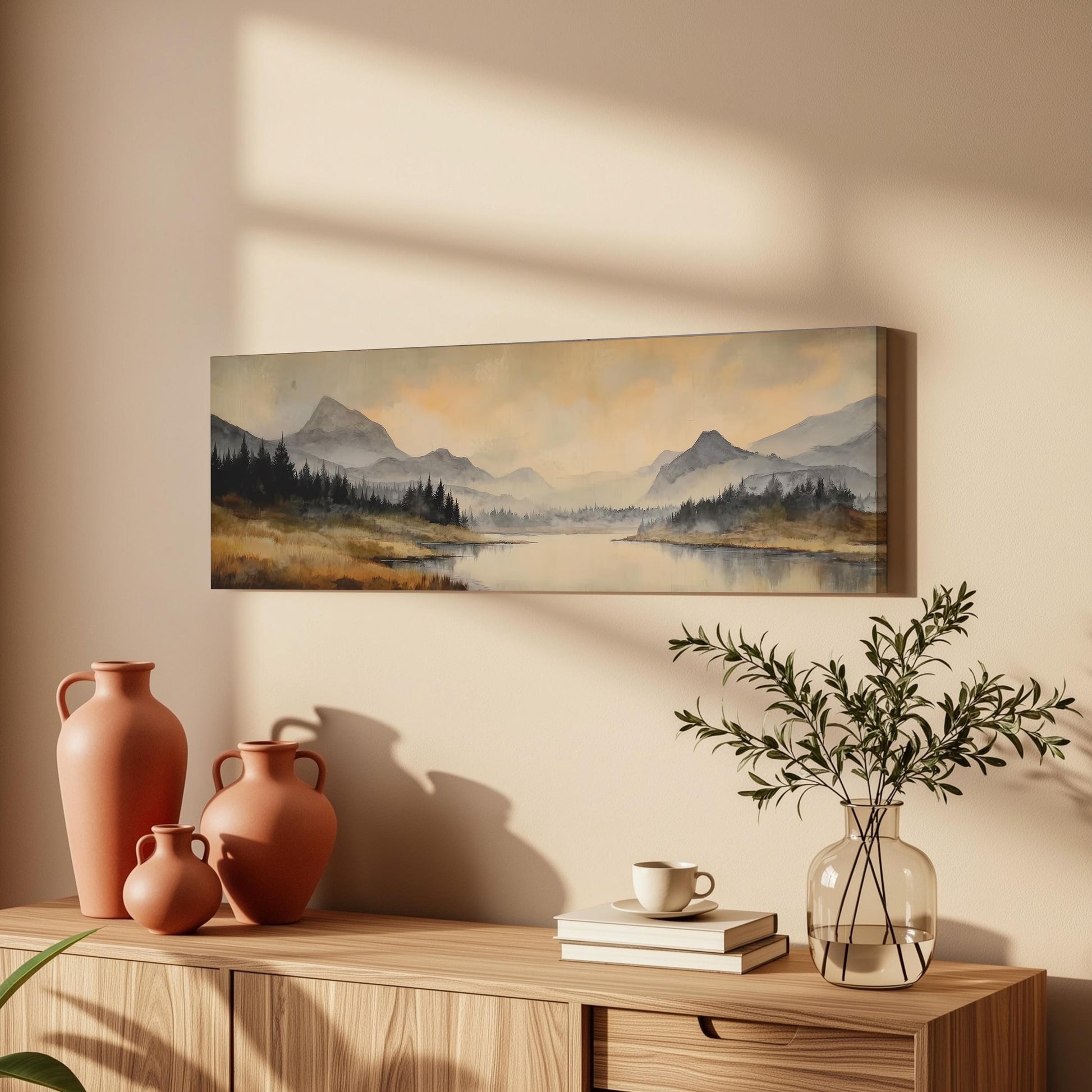 a wooden cabinet with a painting of a mountain landscape hanging on the wall above it. The cabinet also has three orange vases and a glass vase with greenery, as well as a stack of books and a cup on the surface.