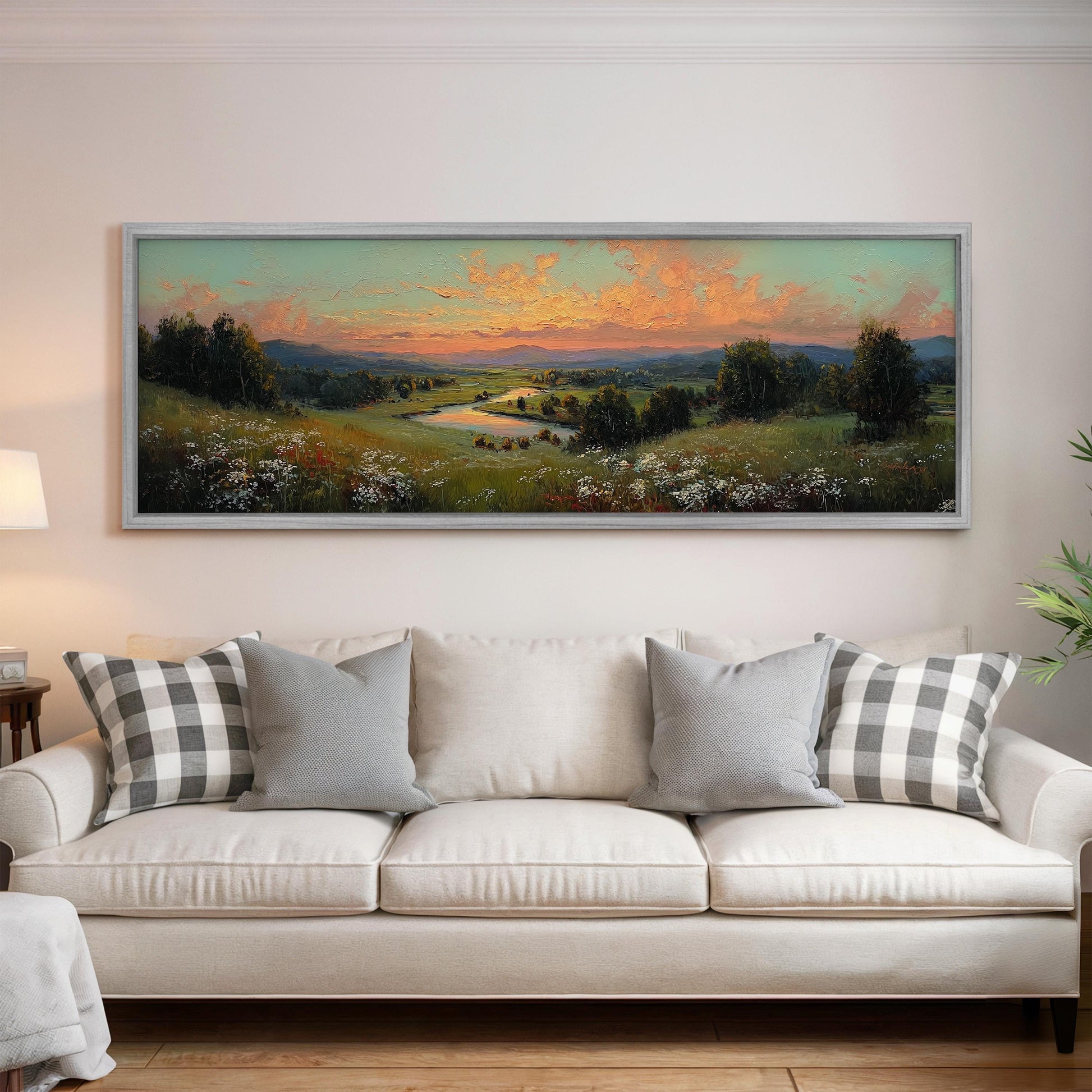 a large, framed landscape painting hanging on a wall above a white sofa with gray and white patterned pillows.