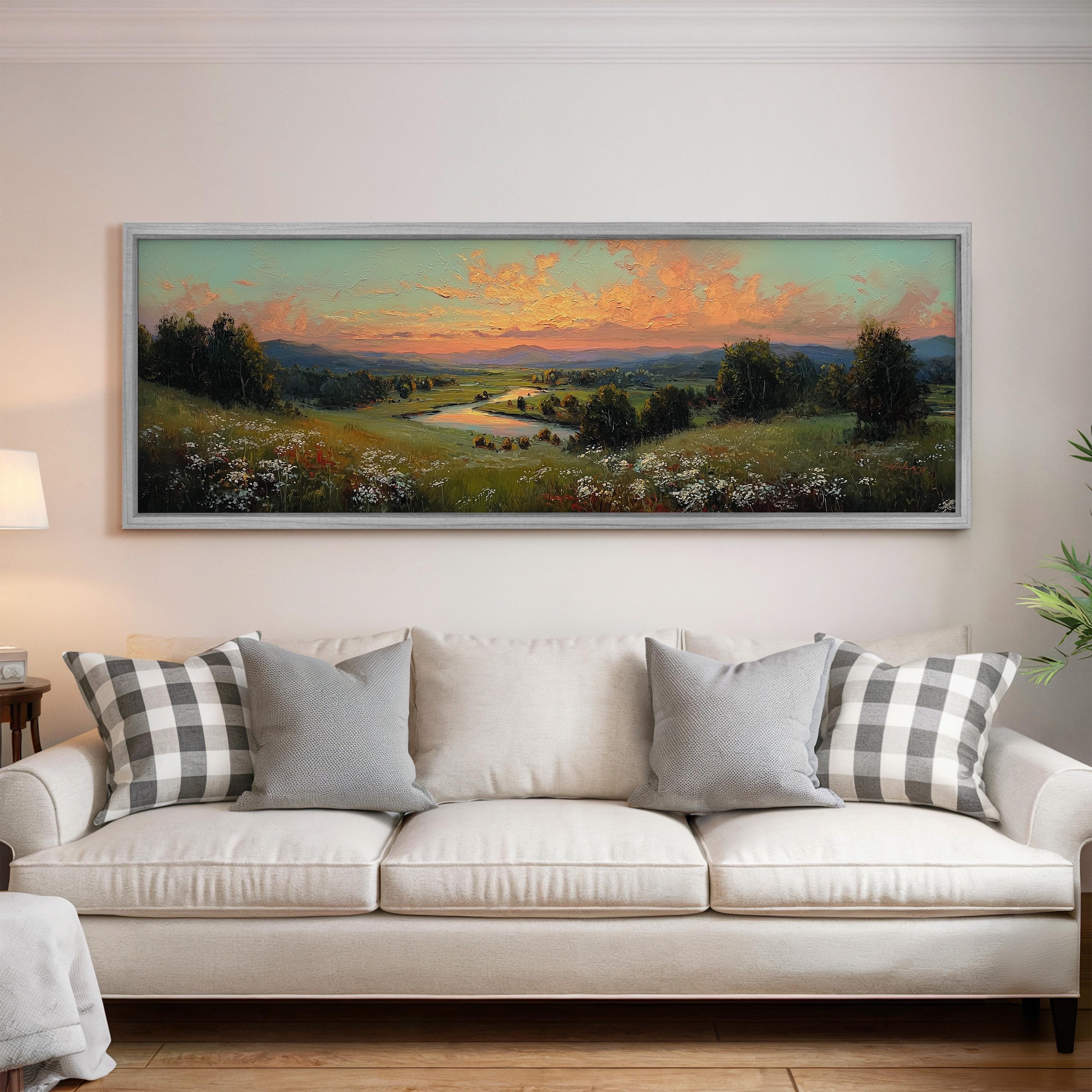 a large, framed landscape painting hanging on a wall above a white sofa with gray and white patterned pillows.
