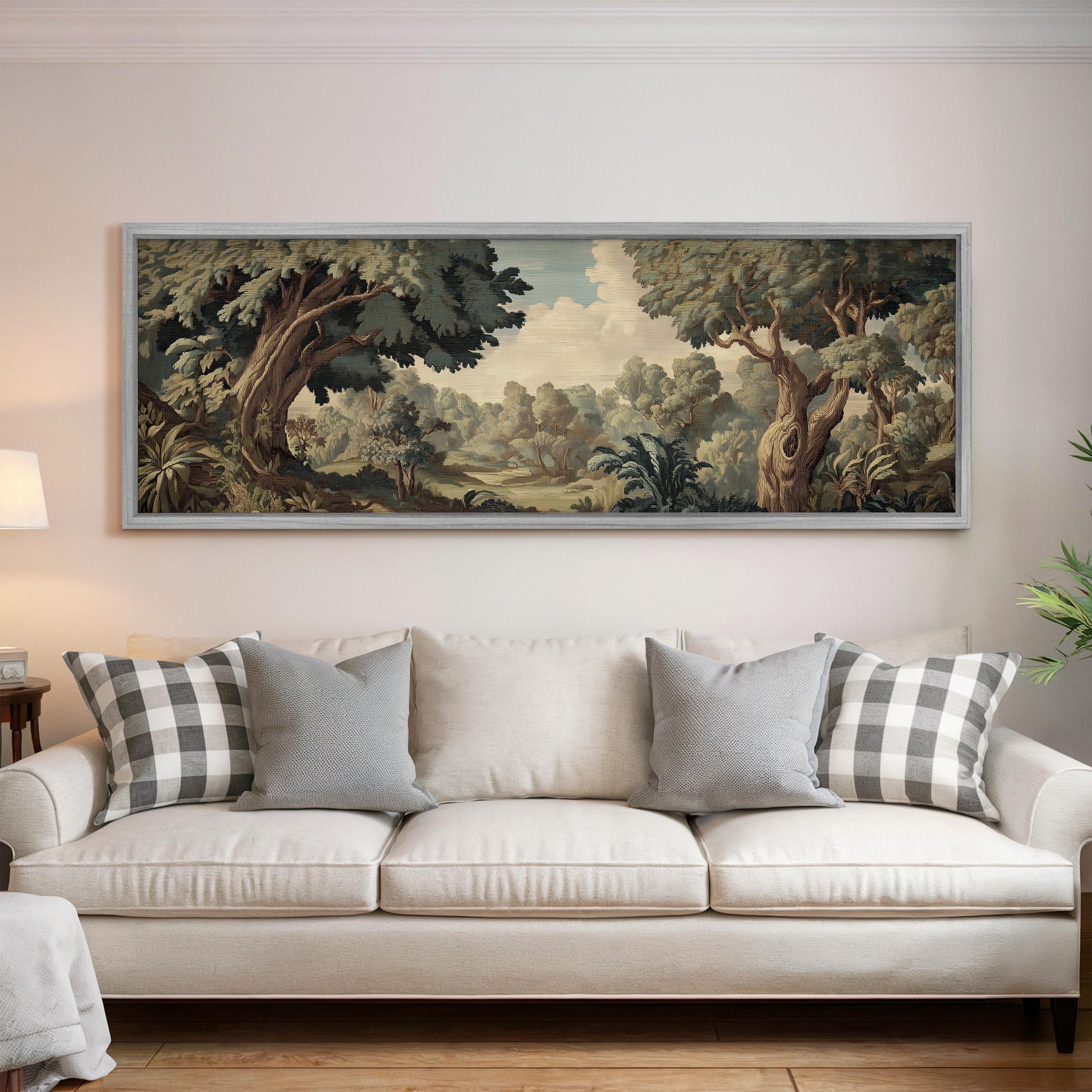 a large, framed painting of a lush, forested landscape hanging on a wall above a white sofa with gray and white patterned throw pillows.