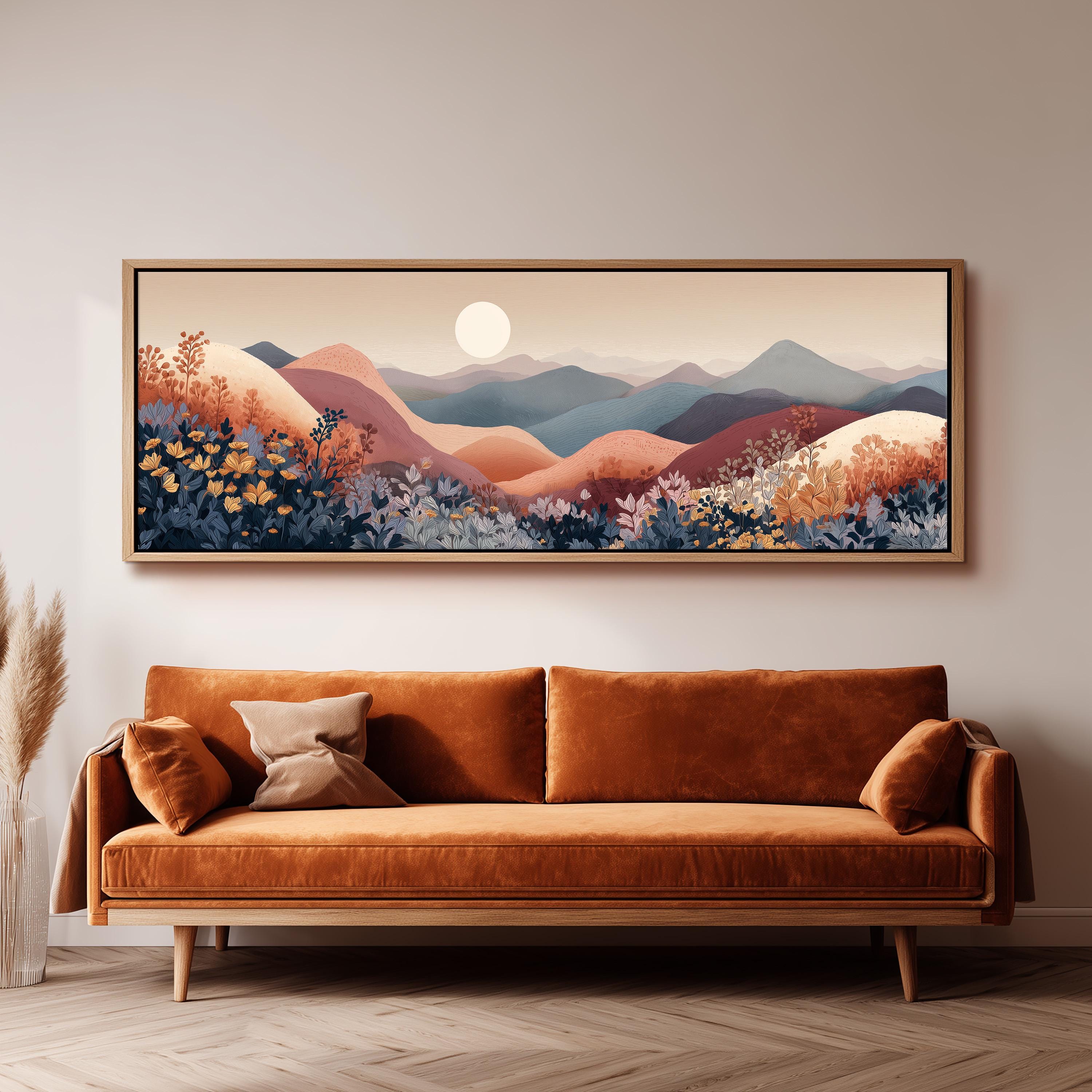 a large, framed painting of a mountainous landscape with a sun in the sky, hanging on a wall above a brown sofa with orange cushions.