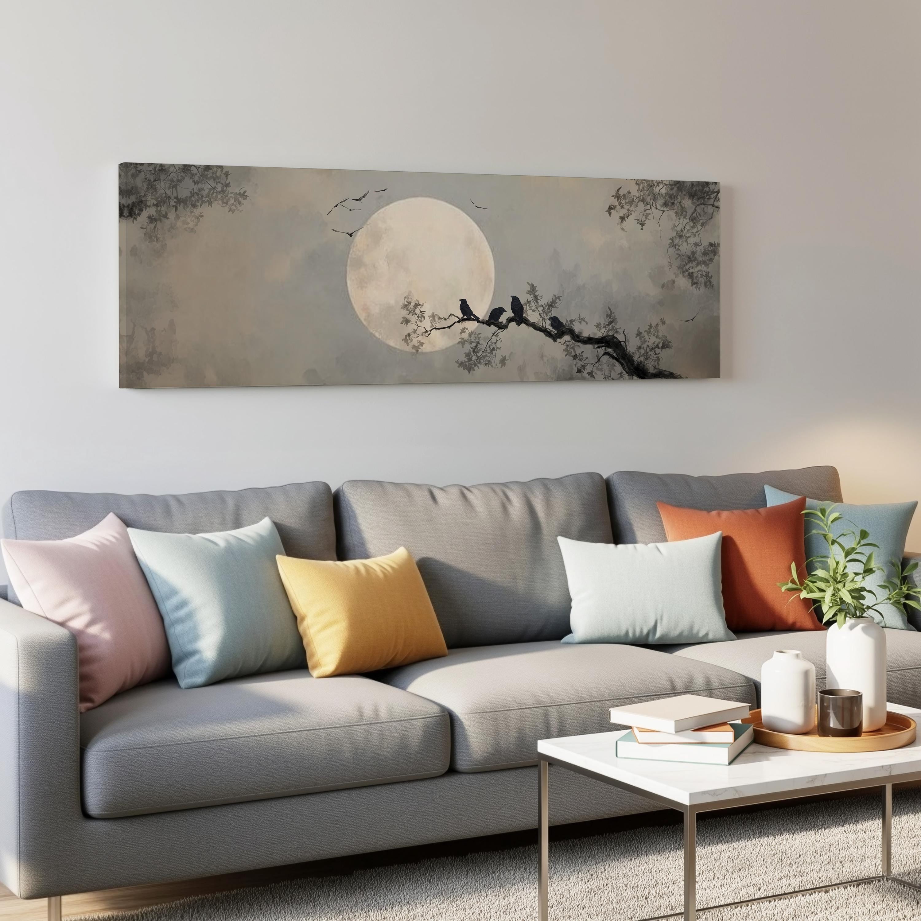 a gray couch with colorful throw pillows, a coffee table, and a large wall art depicting a moonlit night scene with birds perched on a tree branch.